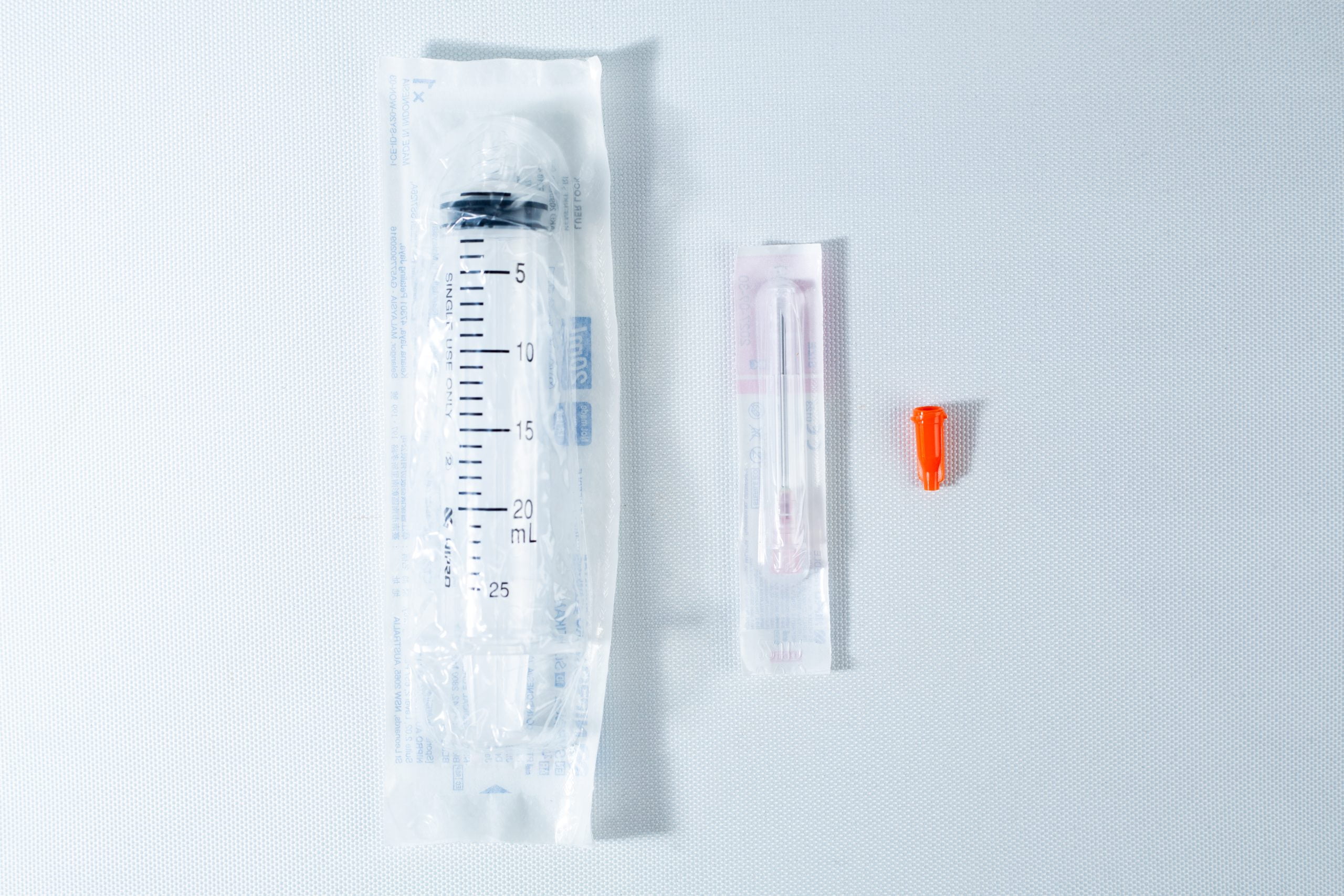 Syringes Luer lock with Hypodermic Needle and syringe Cap set 2 A packaged syringe, a packaged needle, and an orange needle cap on a white surface.