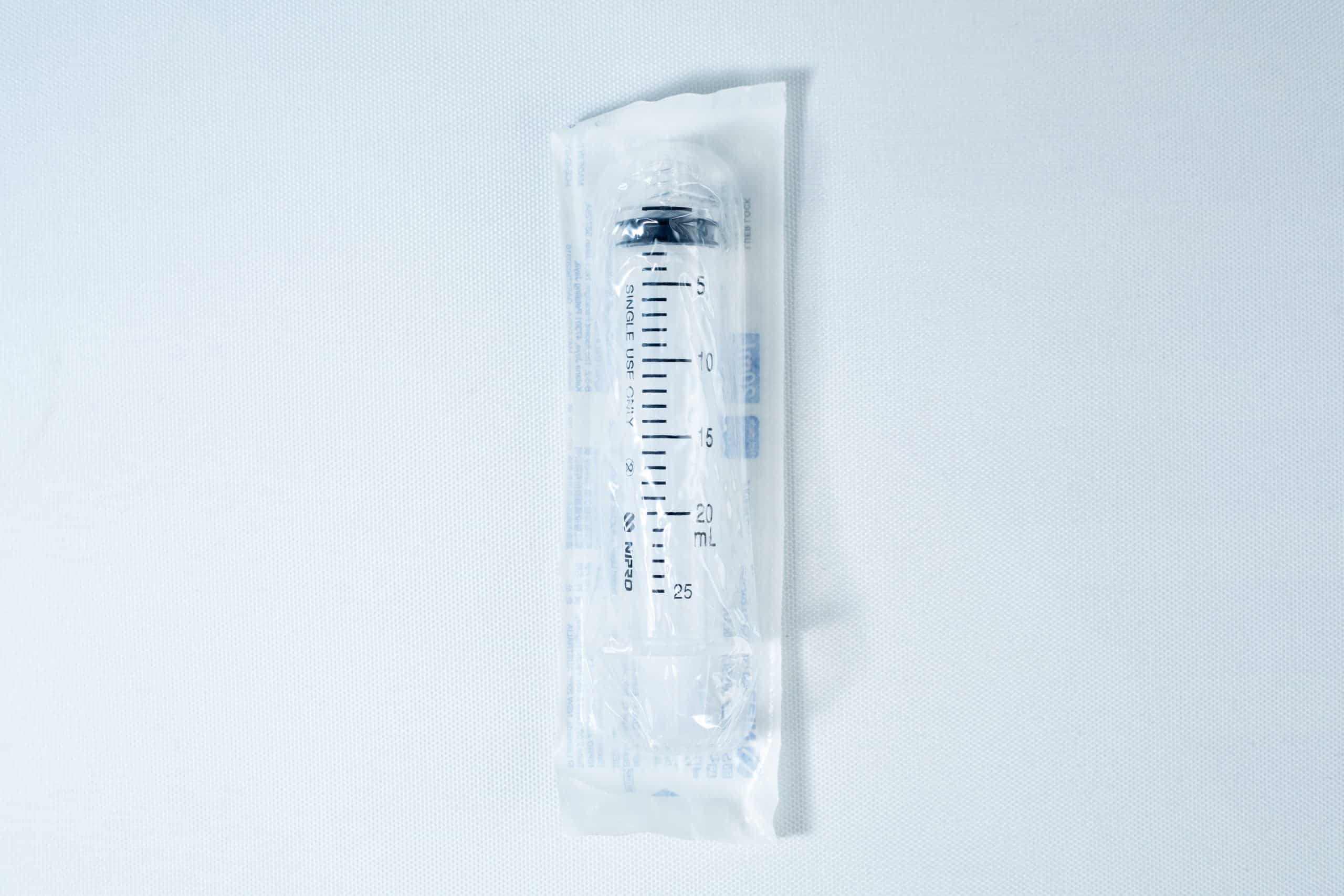Syringes Luer lock with Hypodermic Needle and syringe Cap set 4 A packaged disposable syringe lies on a white surface, sealed in transparent plastic wrapping.