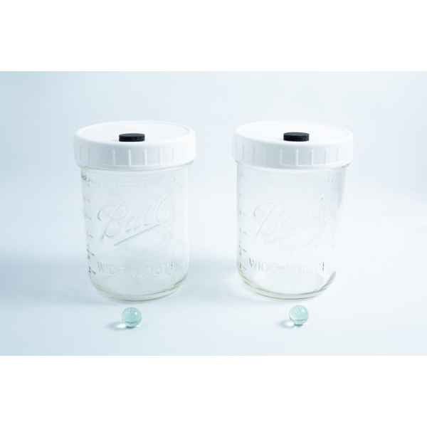 Two empty Mycology Ball Mason jars with injection ports and air vents, 1L genuine autoclavable, sit side by side, green marbles in front on a clean white background.