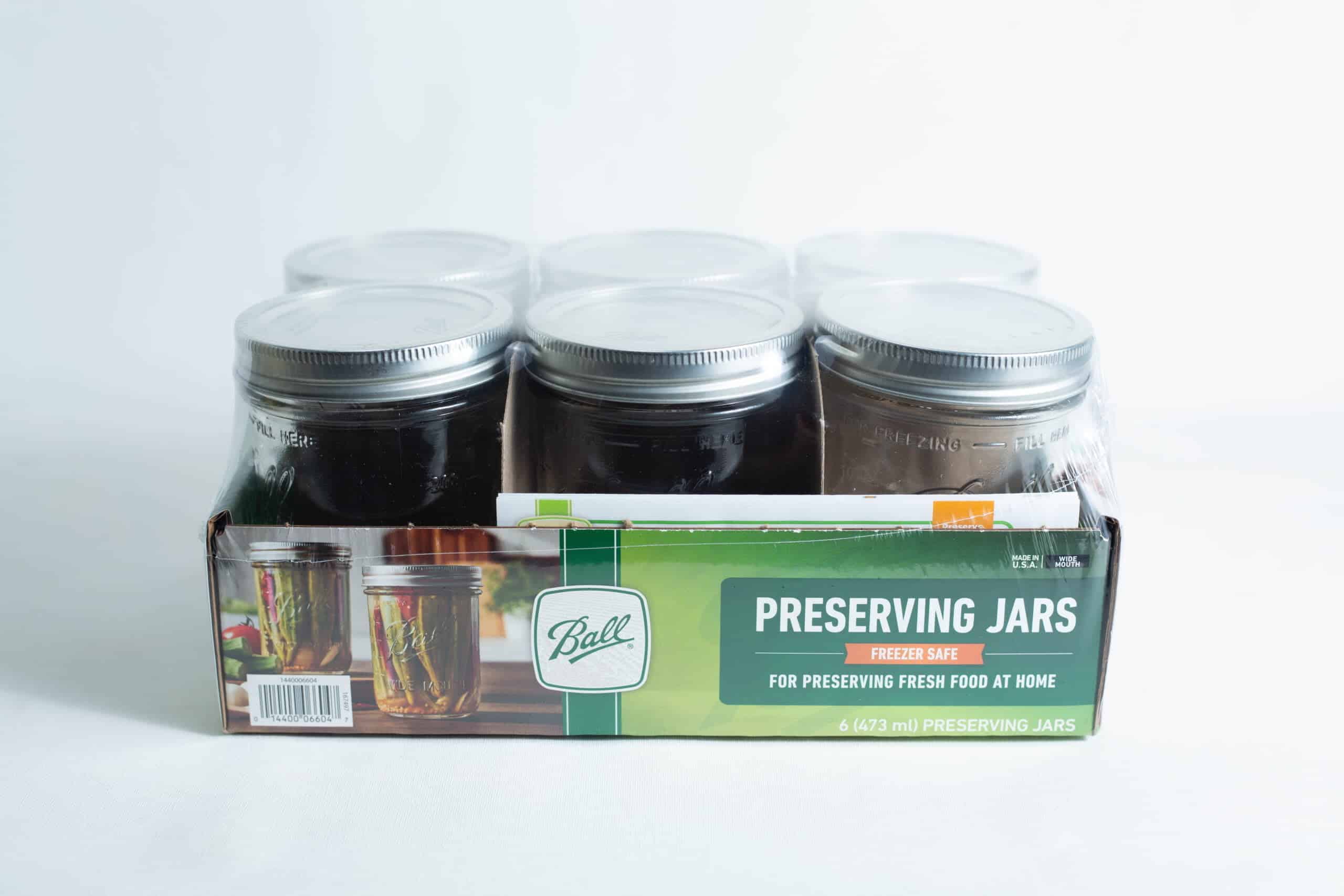 Ball mason pint jars wide mouth set of 6 1 A set of six Ball Mason pint jars with wide mouths are organised in a cardboard box labelled "Preserving Jars" and shown against a white background.