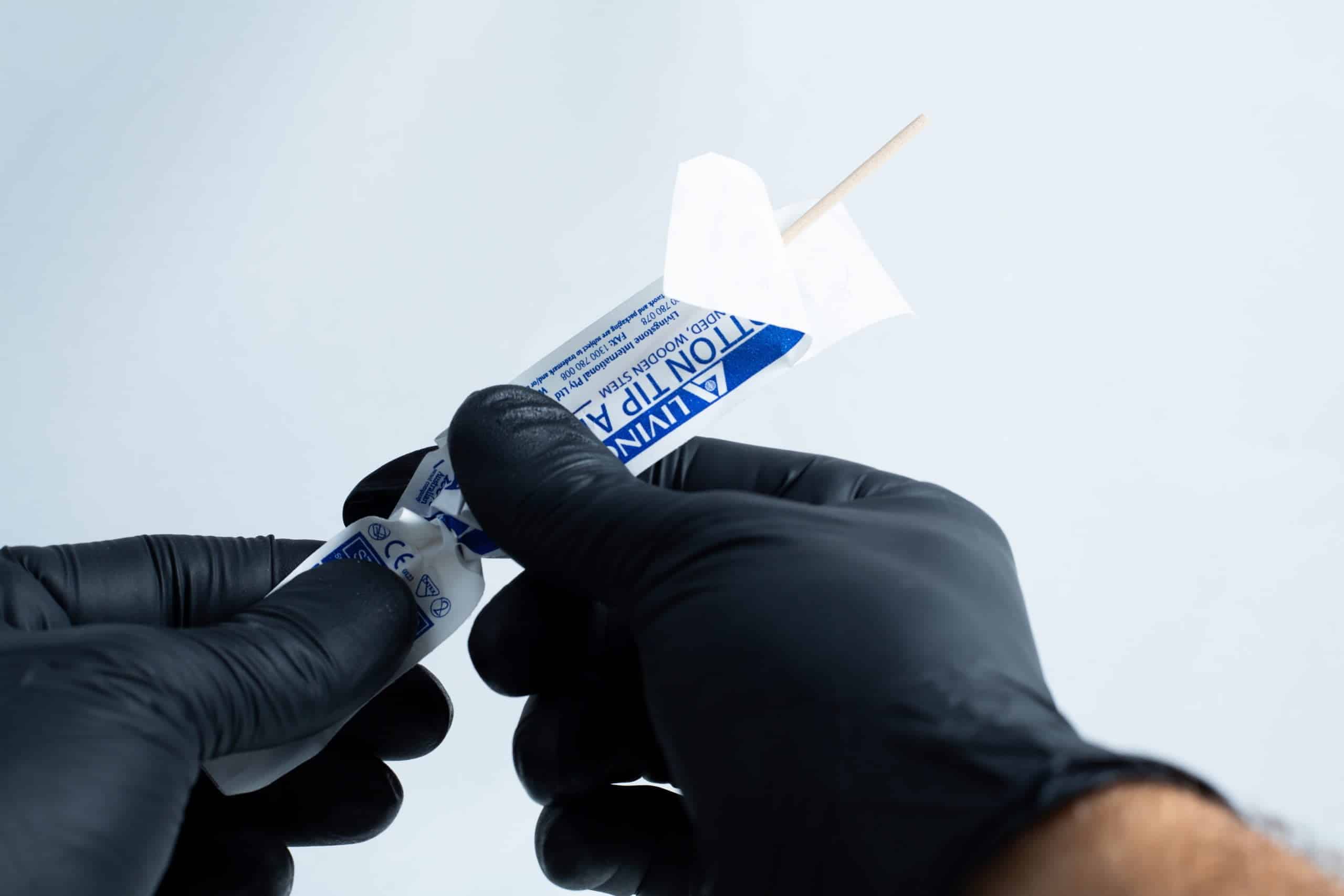 Agar petri dish MEA School Science Fun Project Kit 3 Gloved hands open a sterile wooden tongue depressor from its packaging, ready to use with the Agar petri dish MEA School Science Fun Project Kit for school experiments.