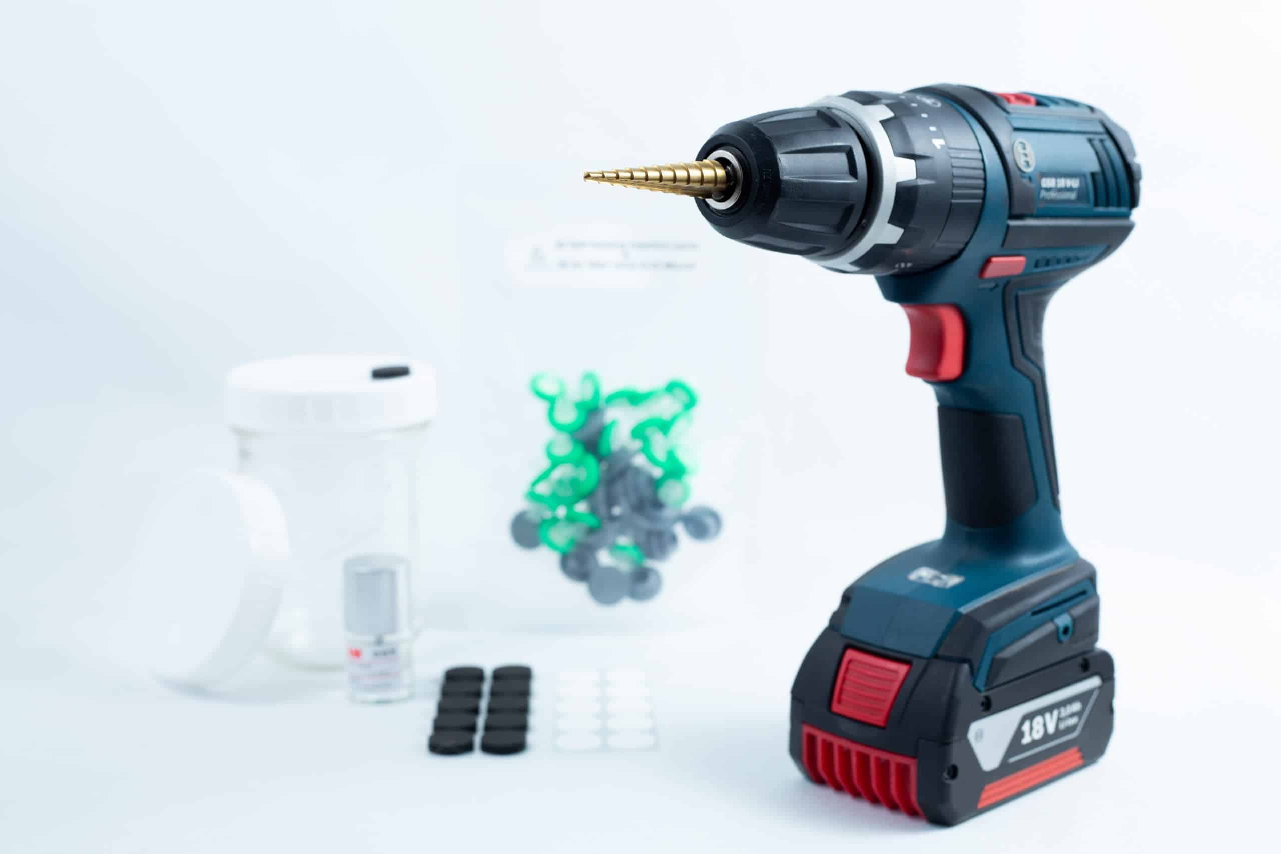 Drill Bit for holes size 3mm-12mm Titanium Coated 5 A Drill Bit for holes size 3mm–12mm Titanium Coated rests beside small containers and plastic pieces on a white surface.