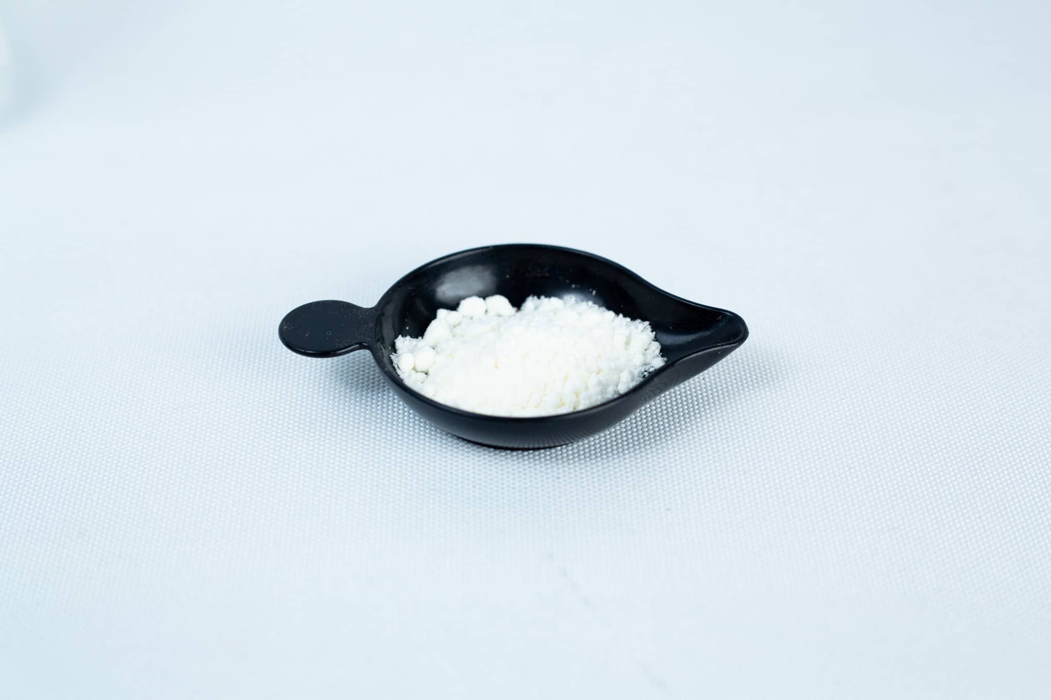 Antibacterial Powder for mushroom cultivation 1 A small black dish holds Antibacterial Powder for mushroom cultivation, seen as a fine white substance on a plain white surface.