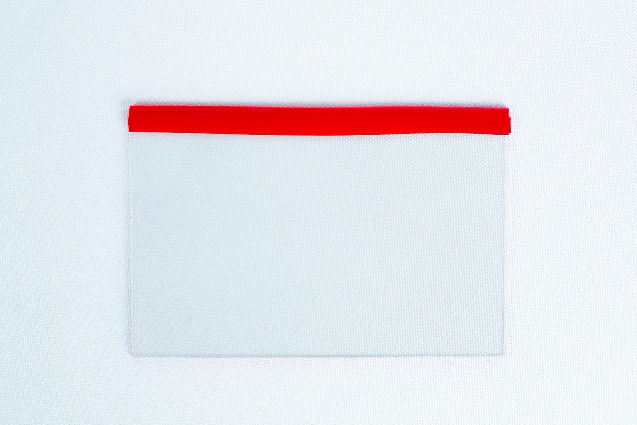 Glass Spore Print Slides booklet 12.8cm X 8.5cm x 1mm 1 A transparent pocket with a red top edge on a white textured background is perfect for storing the Glass Spore Print Slides booklet (12.8cm x 8.5cm x 1mm) to safely preserve spore prints.