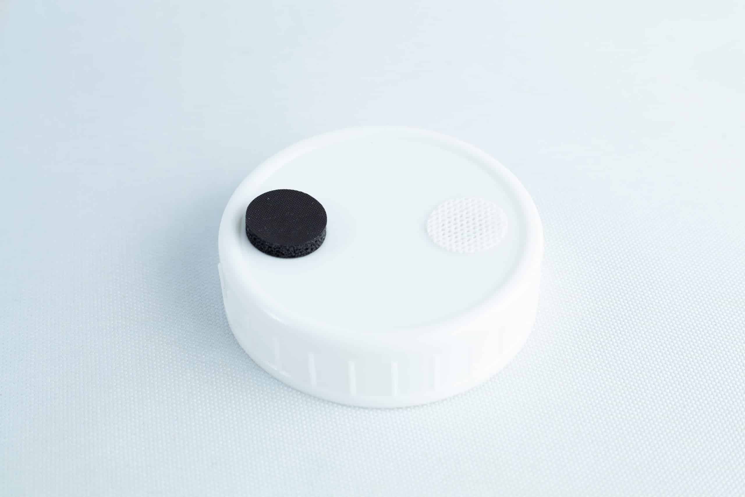 Mycology premade Wide Mouth Mason Jar Lids white with inj port and air filter 6 The Self-healing injection port & Air Vent Filter-3M features a white plastic cap with a black circle and textured white circle on top, designed for secure injections and air venting. Shown against a light background.