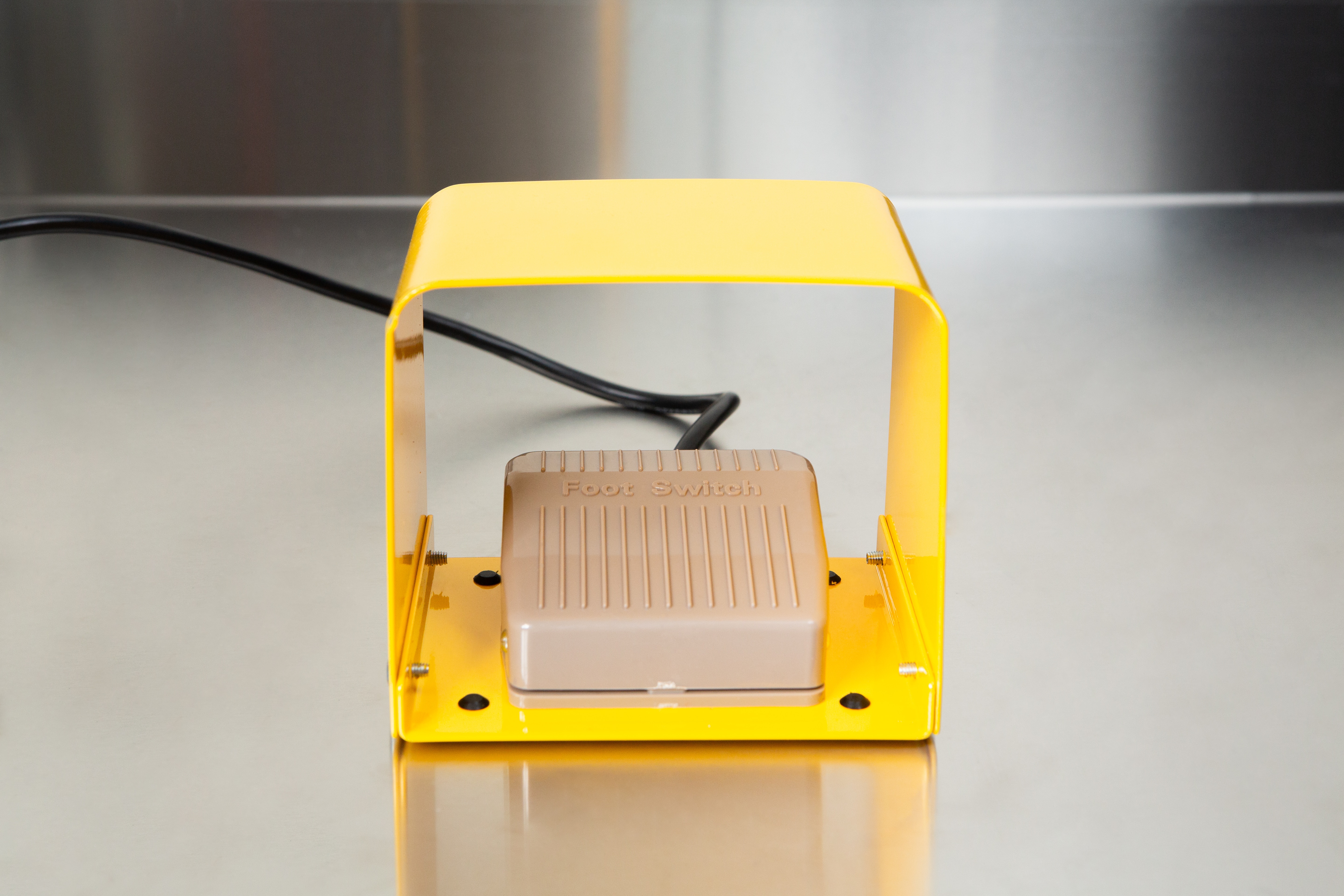 Heat Sealer 450mm with 10mm Seal | Benchtop Model 5 A beige footswitch under a yellow cover rests on a stainless steel surface, ready to operate the Heat Sealer 450mm with 10mm Seal | Benchtop Model.