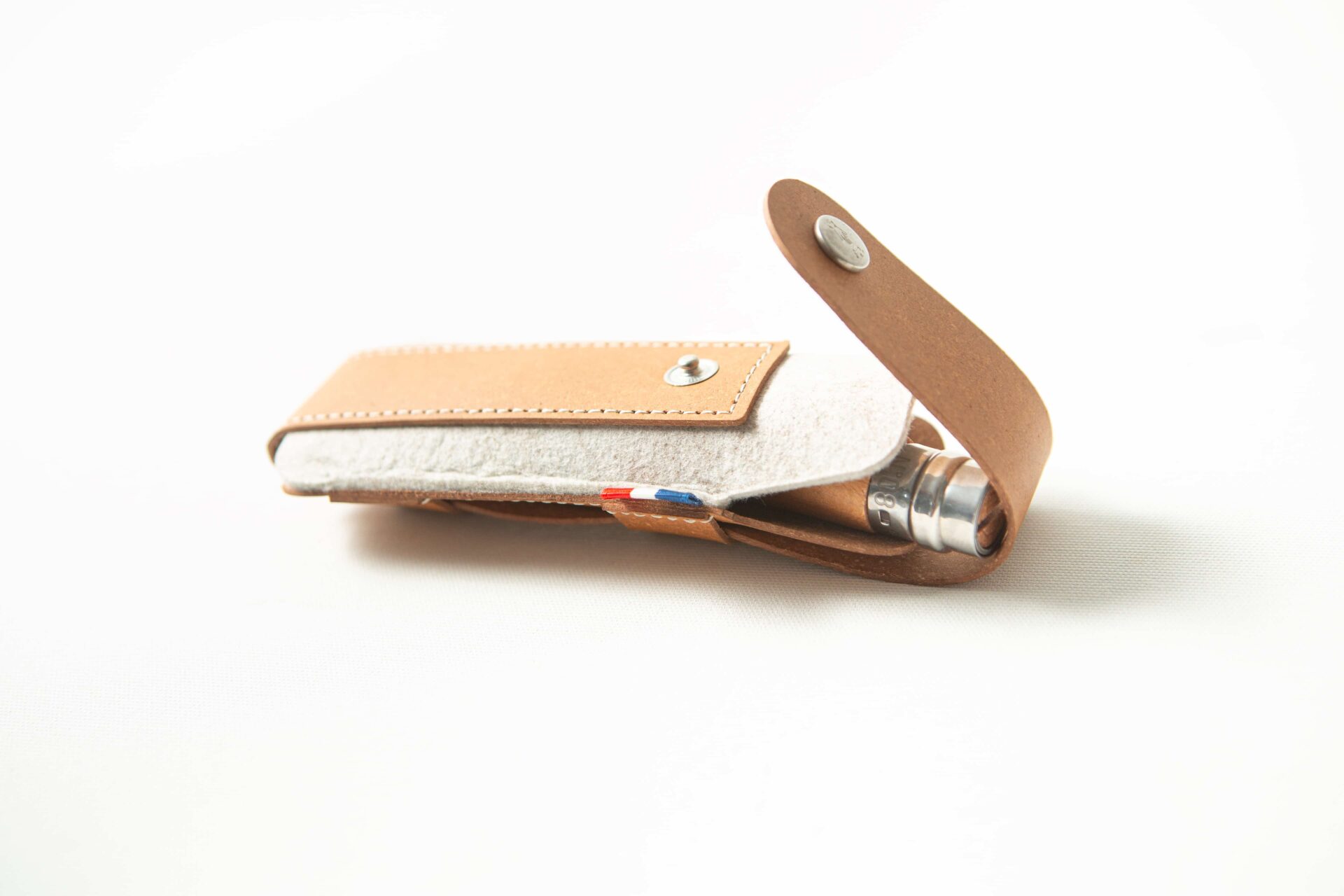 Opinel Sheath - Brown 4 A brown Opinel Sheath, crafted from leather and felt with a press-stud fastening, is partially open to reveal a metal object inside.