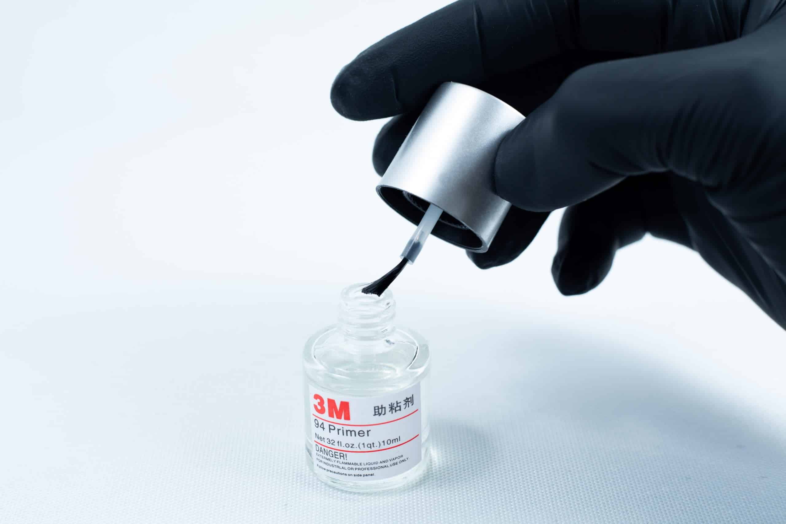 Primer 94 multisurface for 3M glue 10ML 2 A gloved hand holds a brush applicator over an open bottle of Primer 94 multisurface for 3M glue 10ml on a white background.