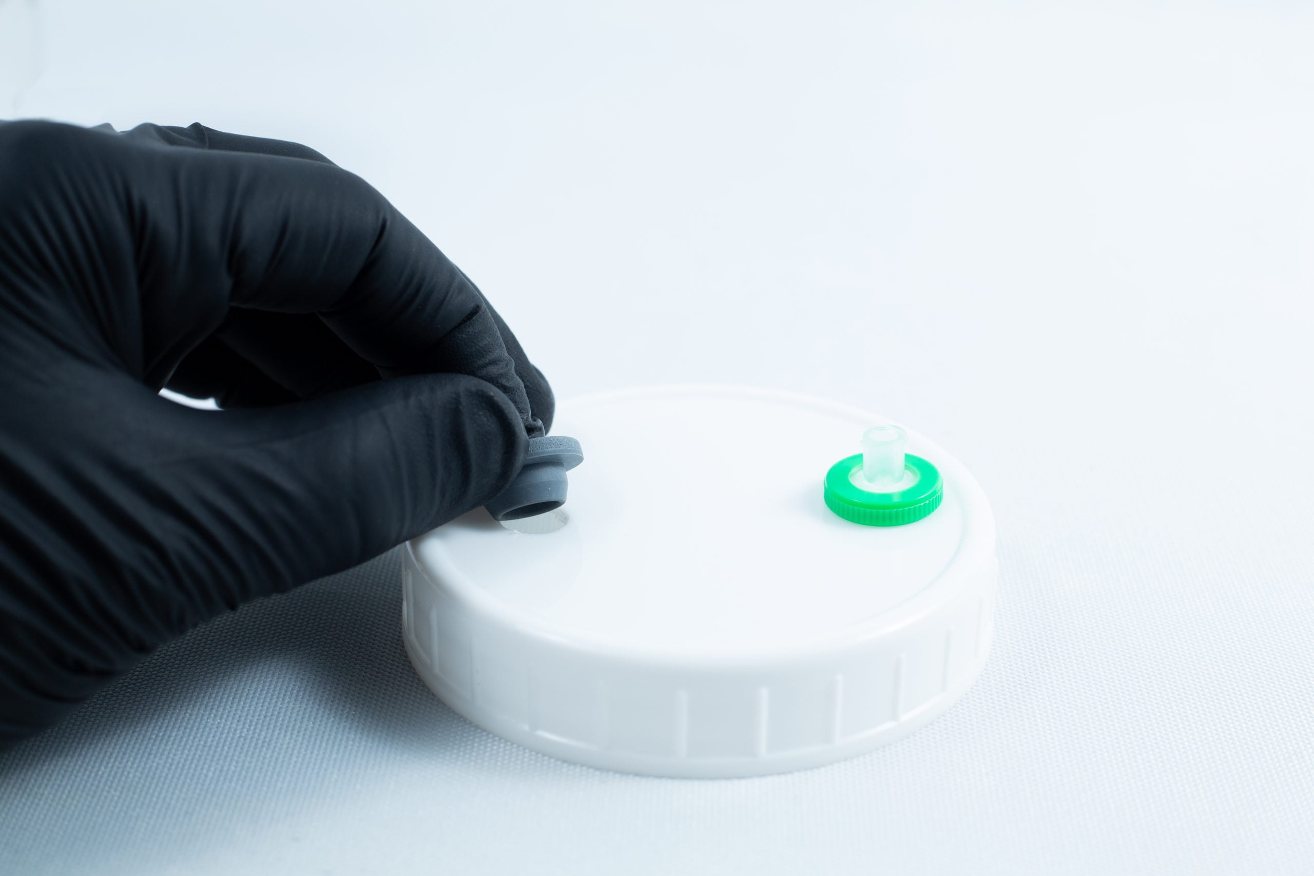 Primer 94 multisurface for 3M glue 10ML 7 A gloved hand holds the grey cap of Primer 94 multisurface for 3M glue 10ML near a white plastic lid with a green port, commonly used as a tape primer on clean white surfaces.