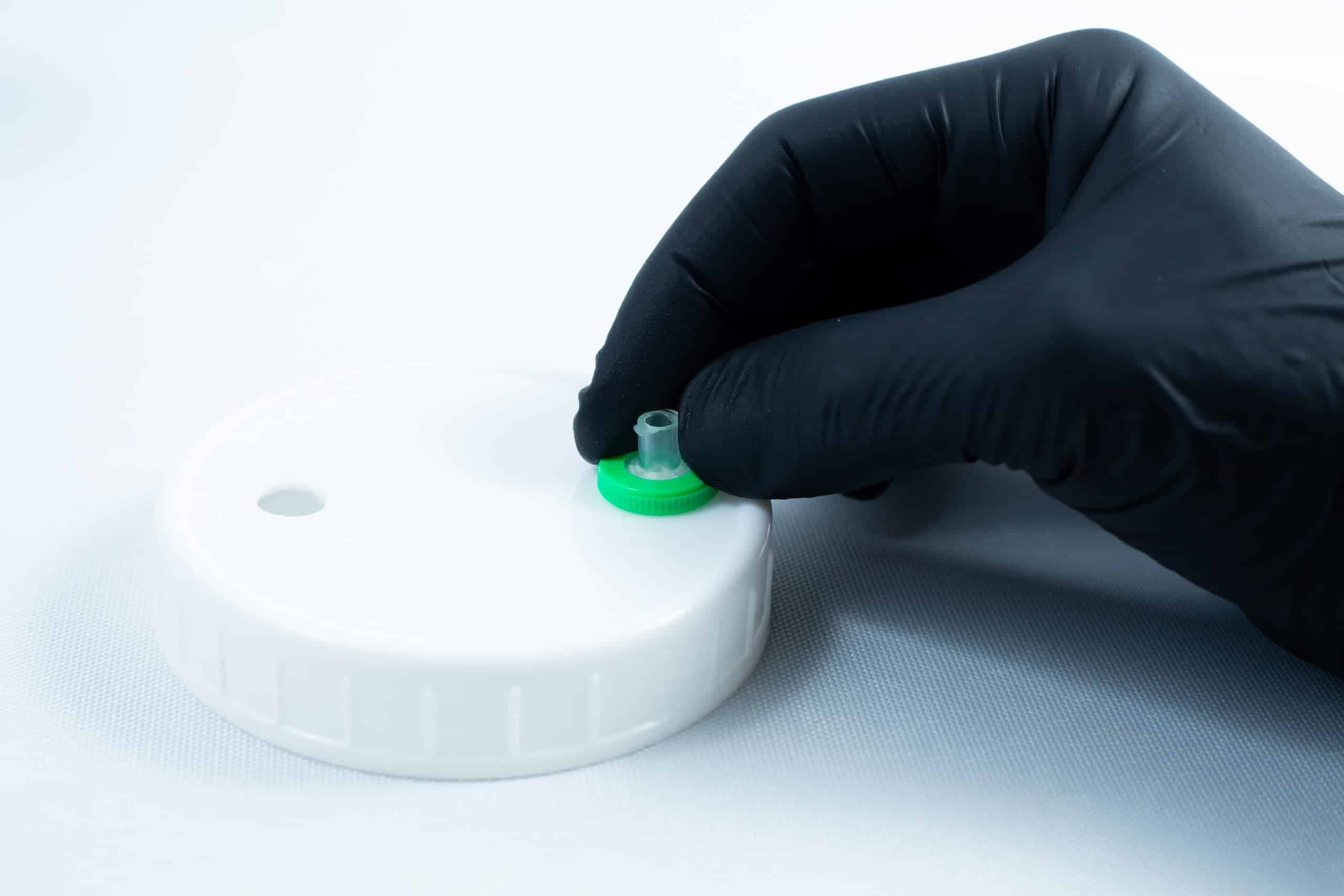 Primer 94 multisurface for 3M glue 10ML 6 A gloved hand holds a green-capped valve on a white plastic lid, commonly used for storing Primer 94 multisurface for 3M glue 10ml, against a white background.