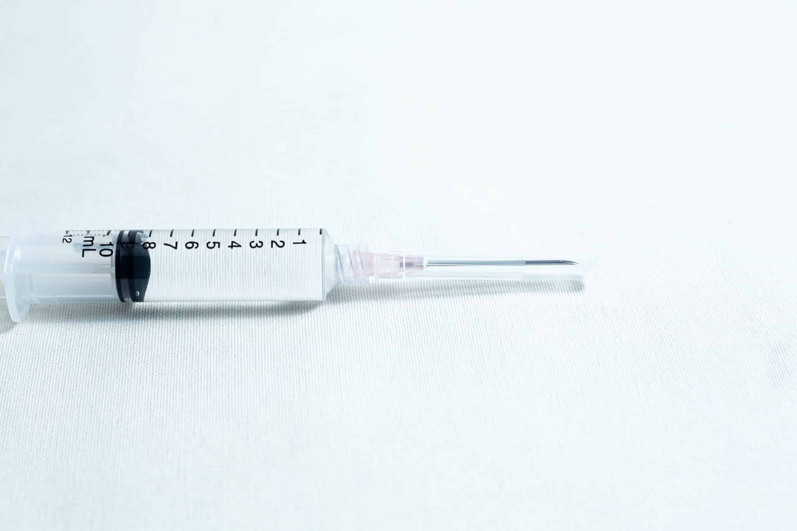 Sterile 18G hypodermic needles whole box 100pcs 9 A syringe with clear liquid rests on a white surface, fitted with a sterile 18G hypodermic needle from a box of 100pcs.