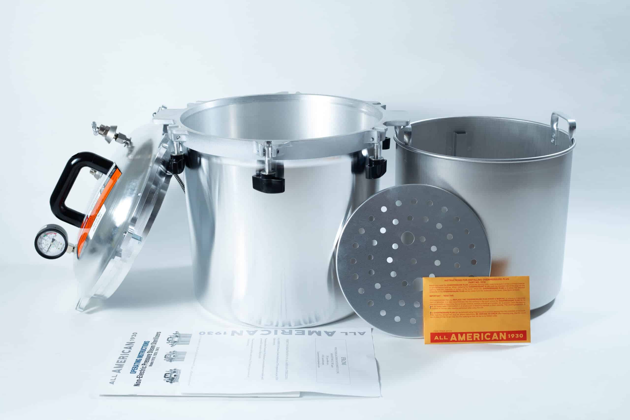 1925x All-American Sterilizer (Autoclave) 25 quart/ 24 Liter 3 A silver pressure cooker with lid, inner pot, rack, instruction manual, and orange card displayed on a white surface.