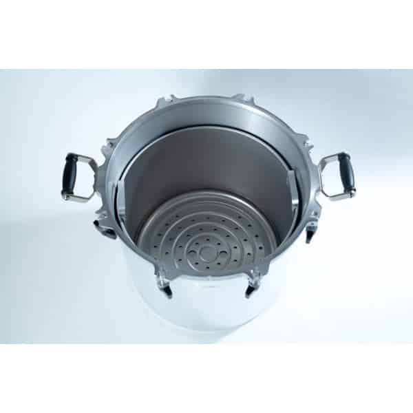 Top view of a large stainless steel pressure cooker with black handles and a perforated metal rack inside.
