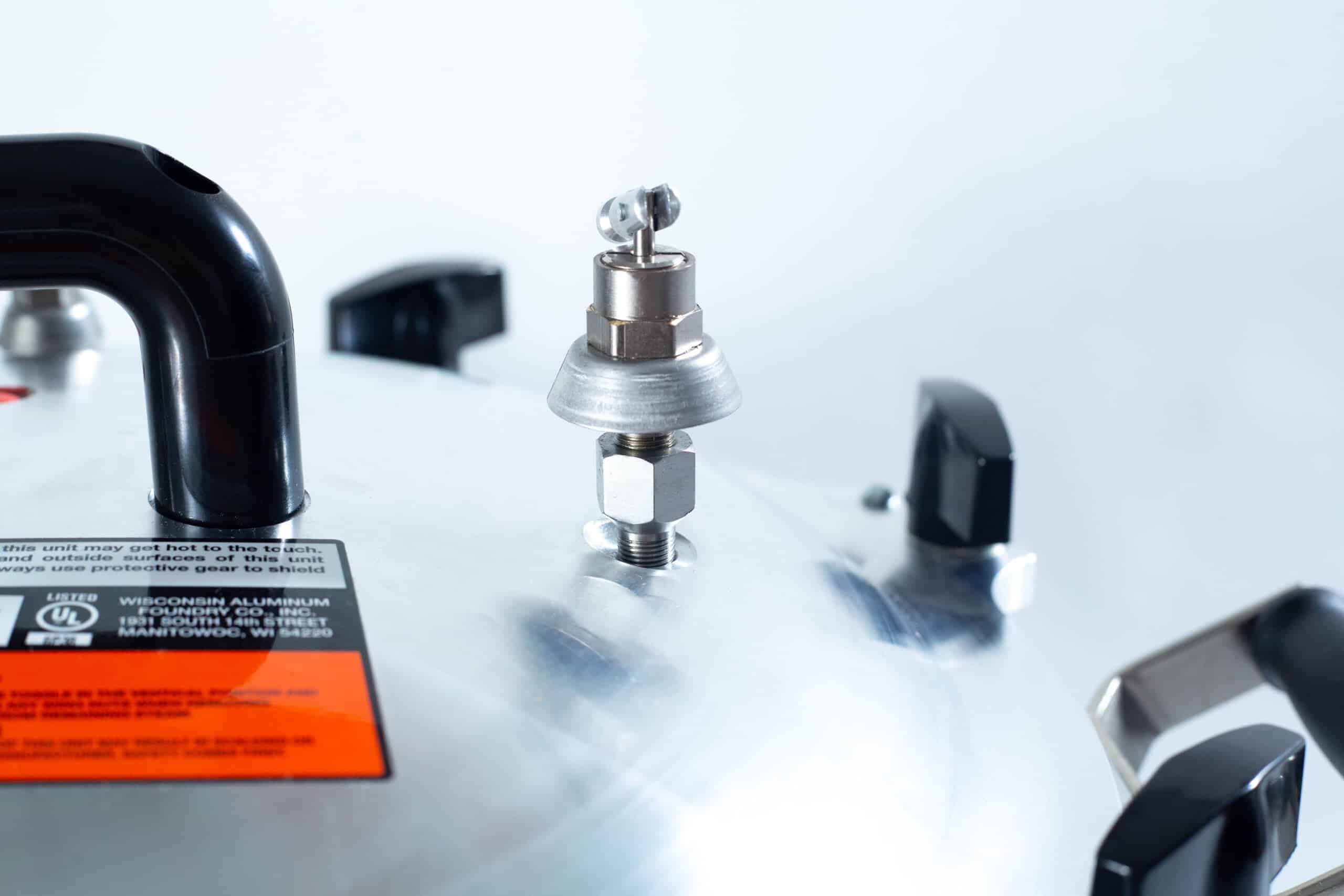 75x All American electric autoclave sterilizer 41 quart 9 Close-up of a pressure cooker lid with a black handle and metal pressure release valve.
