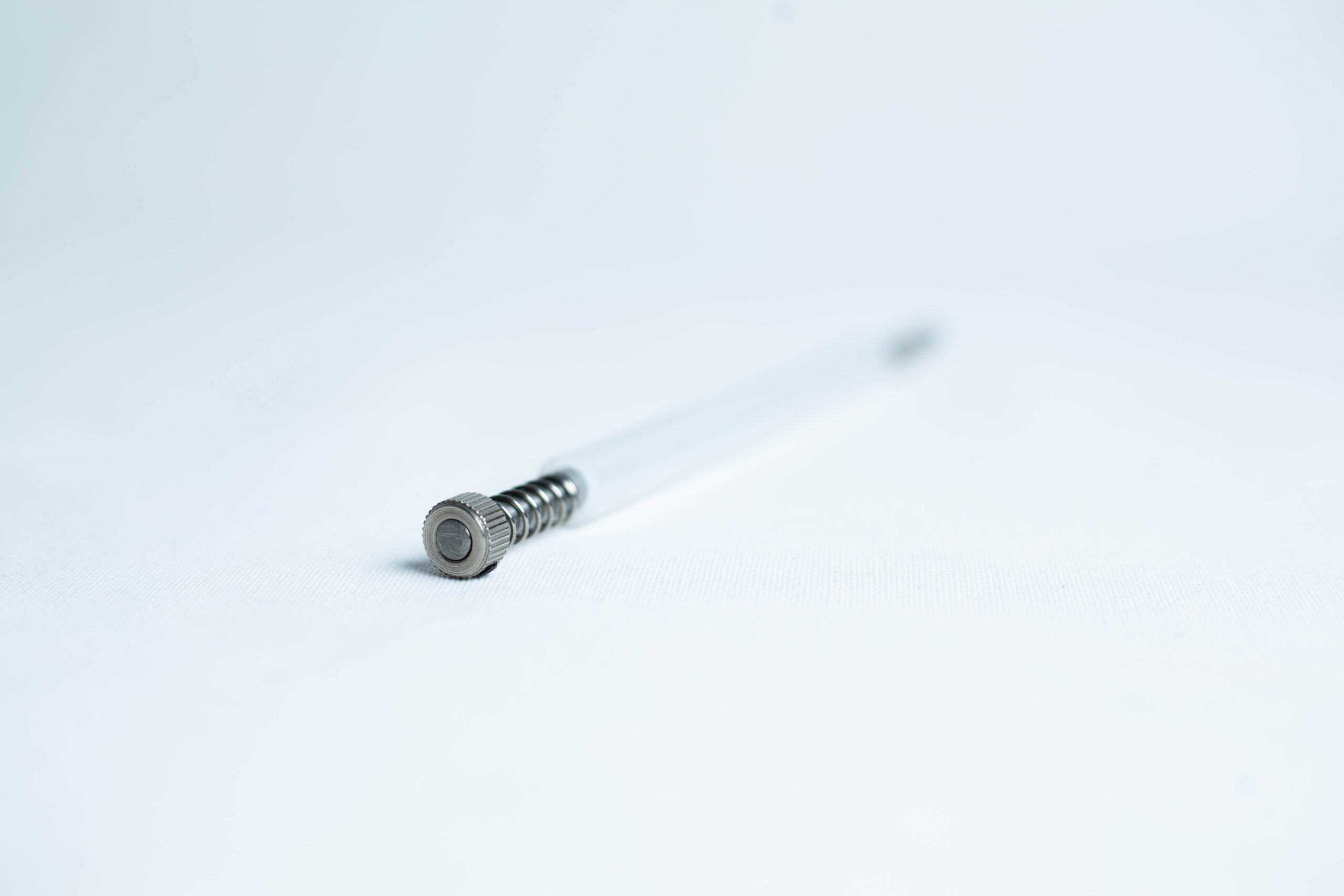 Agar punch transfer tool 2 A metal spring pen refill lying on a white surface, photographed with a shallow depth of field.