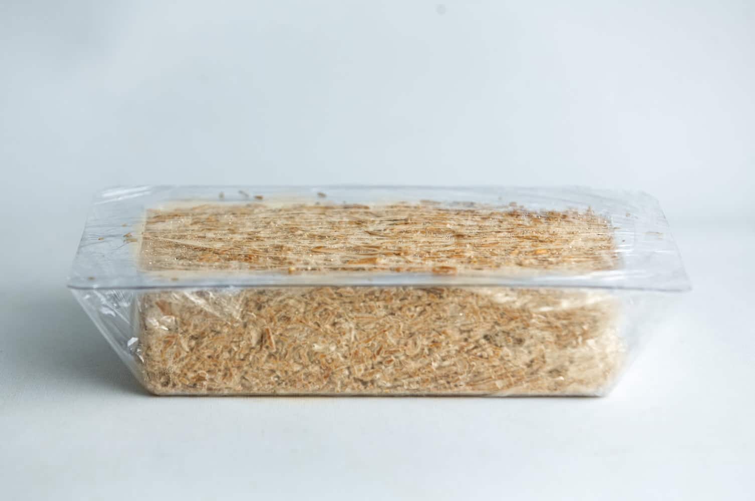 Mycelium Mold Growth form -Brick (Reusable) 11 A block of shredded wheat cereal in a clear plastic tray with a transparent wrapper.