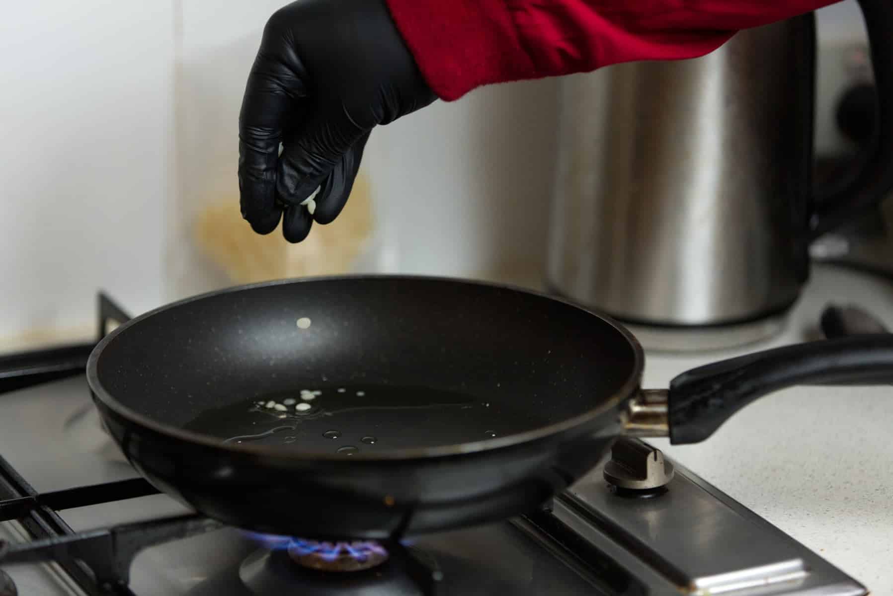 Organic Beeswax 100 gms 2 A gloved hand sprinkles ingredients from the Mushroom Log Kit | Mushroom Inoculation Kit (Sawdust Log) into a frying pan with oil on a lit gas hob.