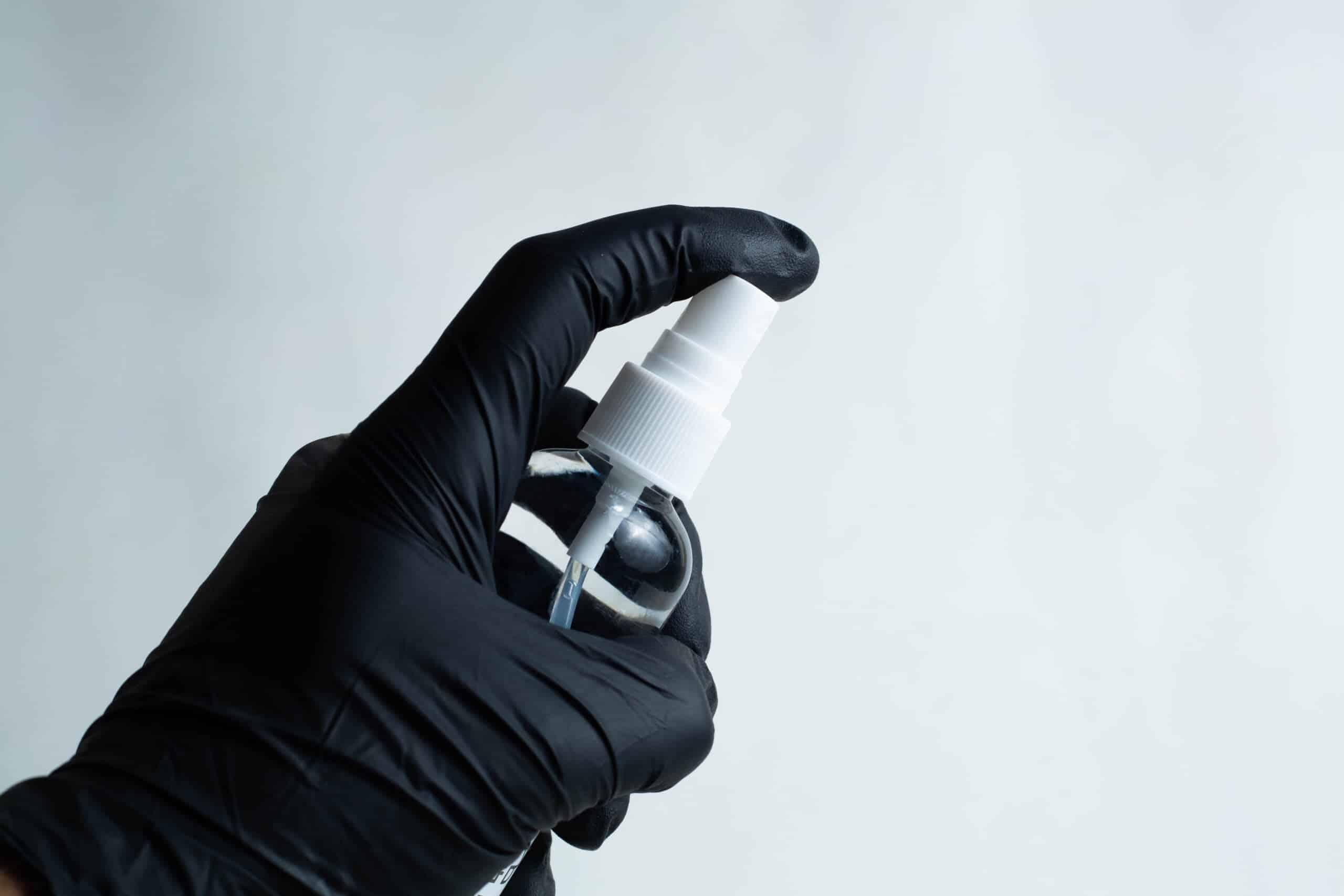 Isopropyl alcohol 70% in 100ml Spray bottle 2 A hand in a black glove holds a 100ml spray bottle of 70% isopropyl alcohol against a plain, light background.