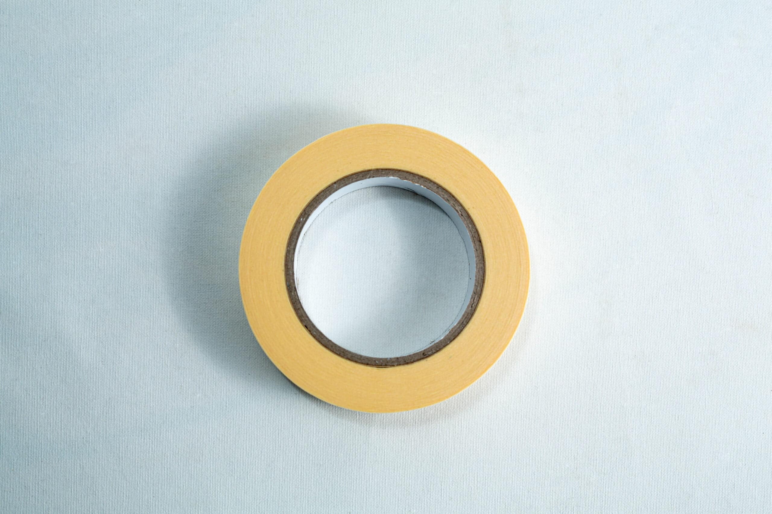 Autoclave sterilization indicator tape 25mm x 50 m 2 A roll of yellow masking tape on a light blue surface, viewed from above.