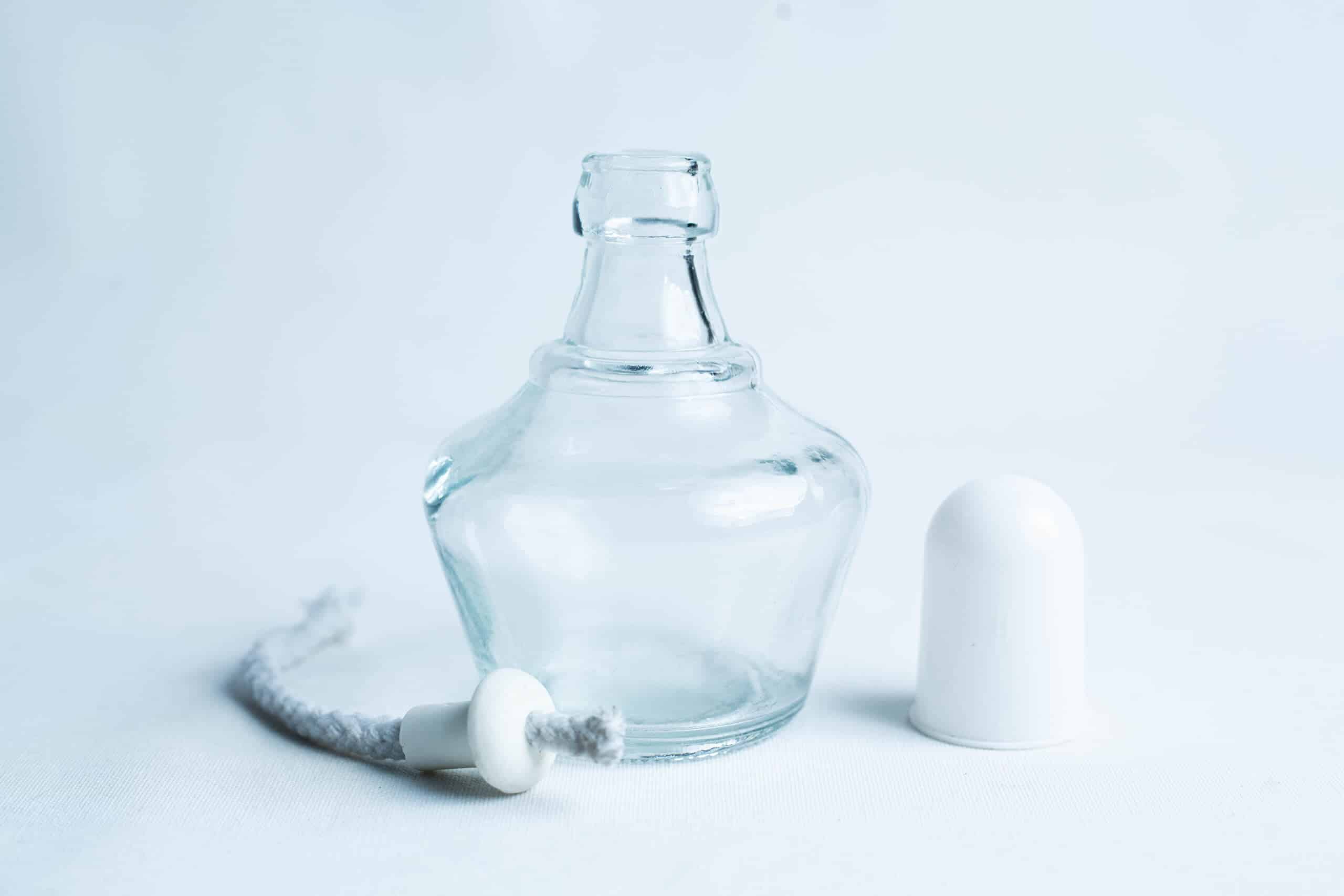 Lamp Spirit glass alcohol burner 150ml 1 A small empty glass bottle with its white cap and a wick placed beside it on a white background.