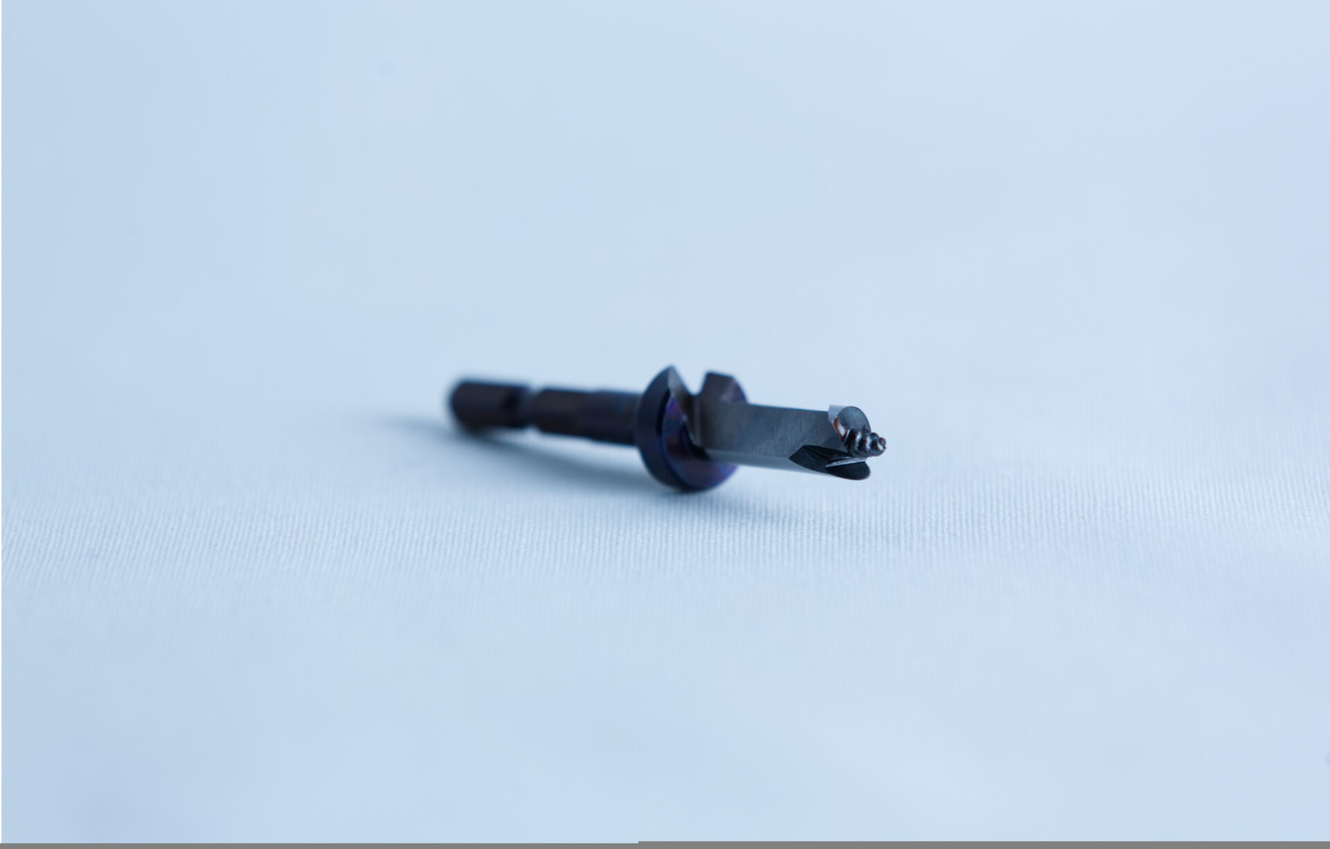 8.5 mm dowel inoculation drill bit with Stopper, Hex shank 2 A close-up of a small metal tool or drill bit on a light blue surface with a blurred background.