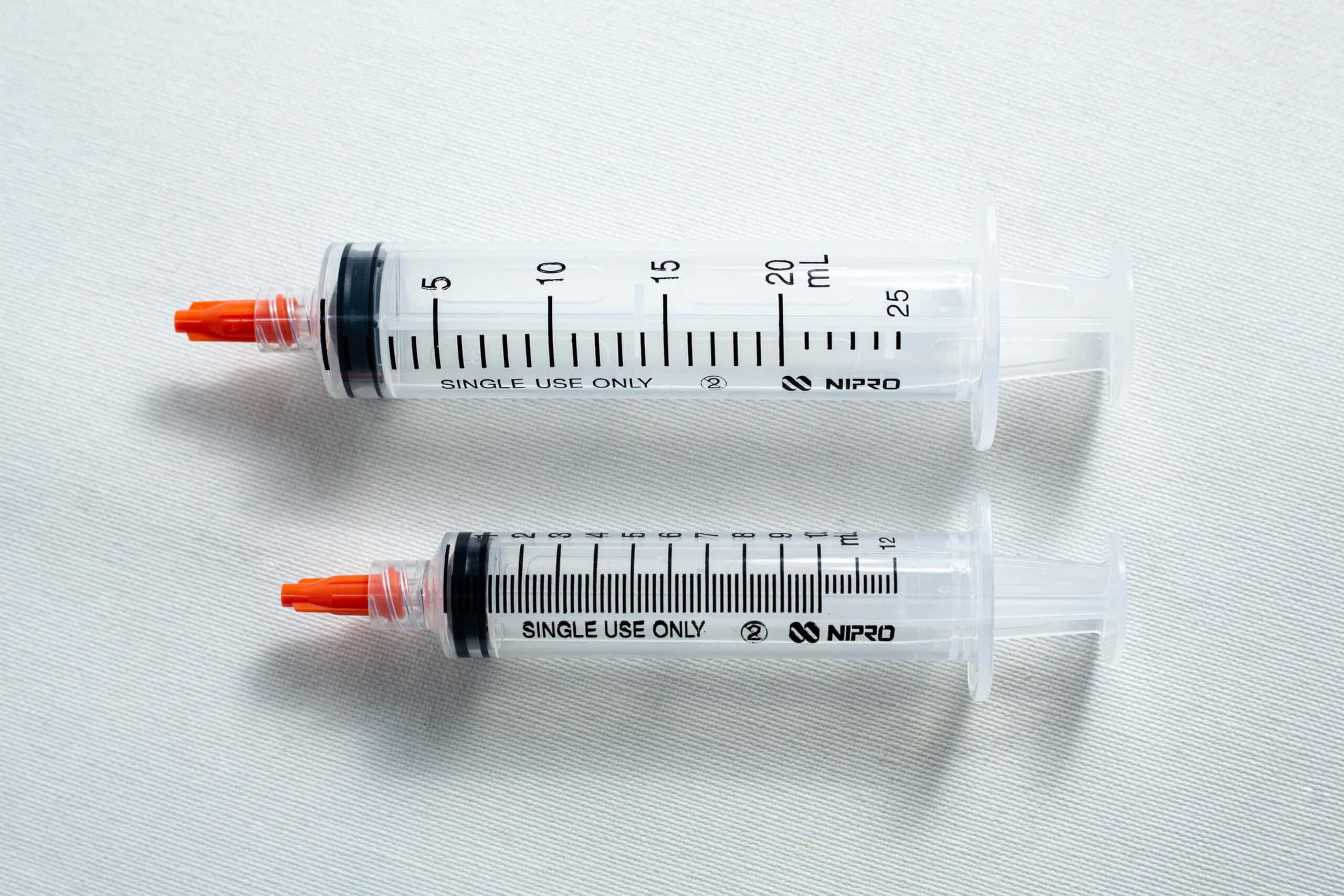 Syringe caps for Luer lock and slip tip 4 Two plastic syringes with orange caps lying side by side on a white surface.