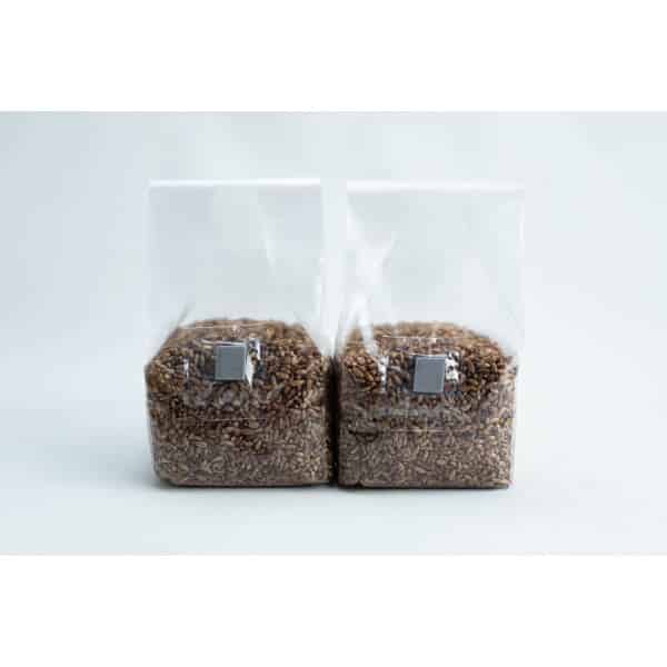 Two clear plastic bags filled with brown grains are placed side by side against a light background.