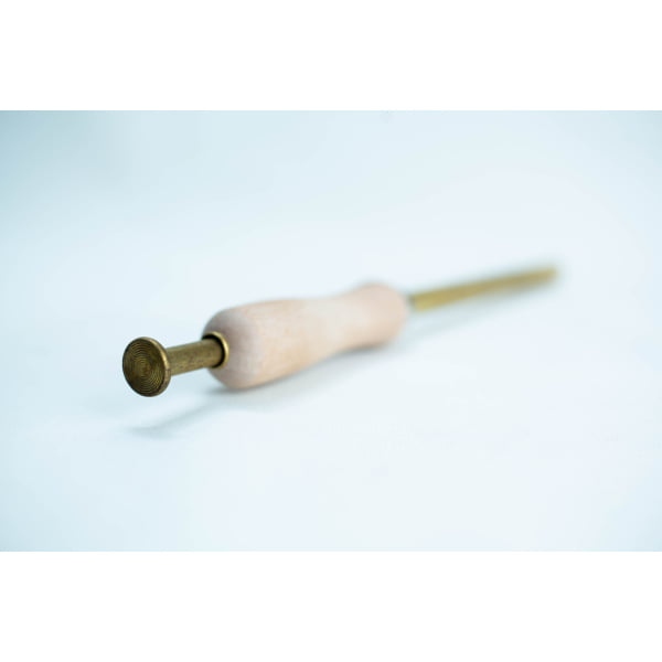 A brass and wooden tool with a round textured tip, lying on a white surface.