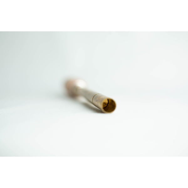 A brass tube with a slightly flared end, lying on a white surface, focussed on the open tip.