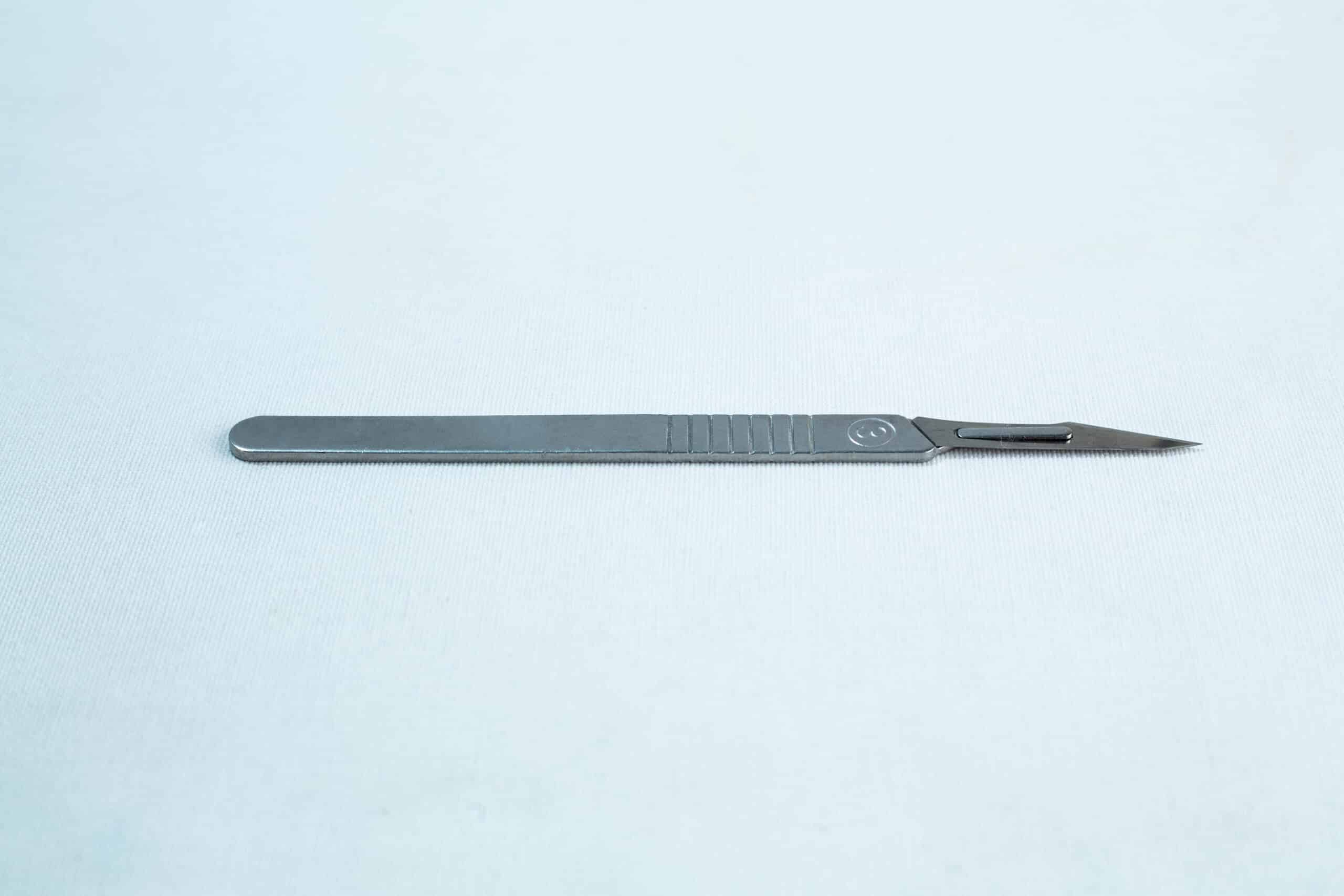 Scalpel handle #3 and blades #11 | Mycology 3 A metal surgical scalpel lies on a plain light surface with its blade facing right.