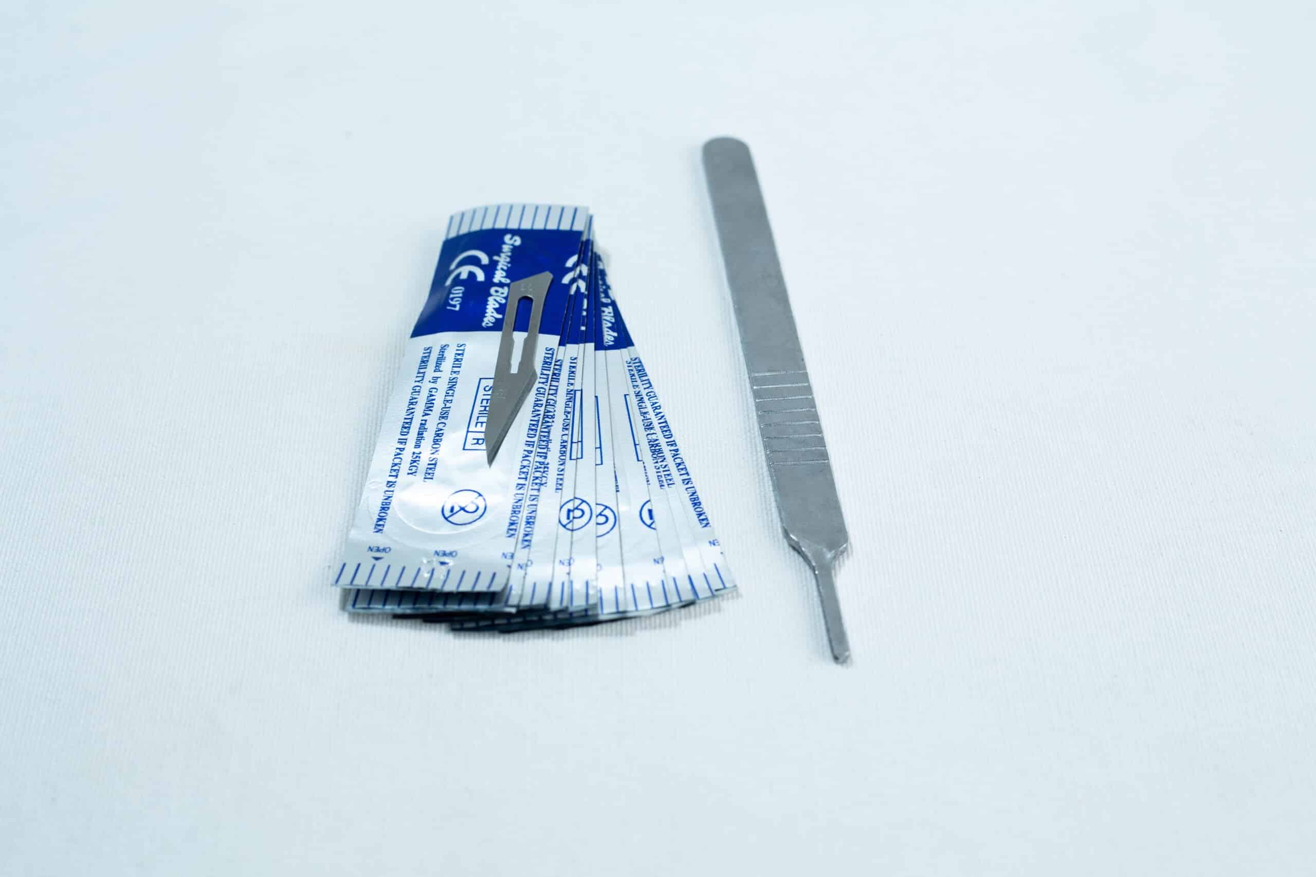 Scalpel handle #3 and blades #11 | Mycology 4 A scalpel handle next to several individually wrapped scalpel blades on a white surface.
