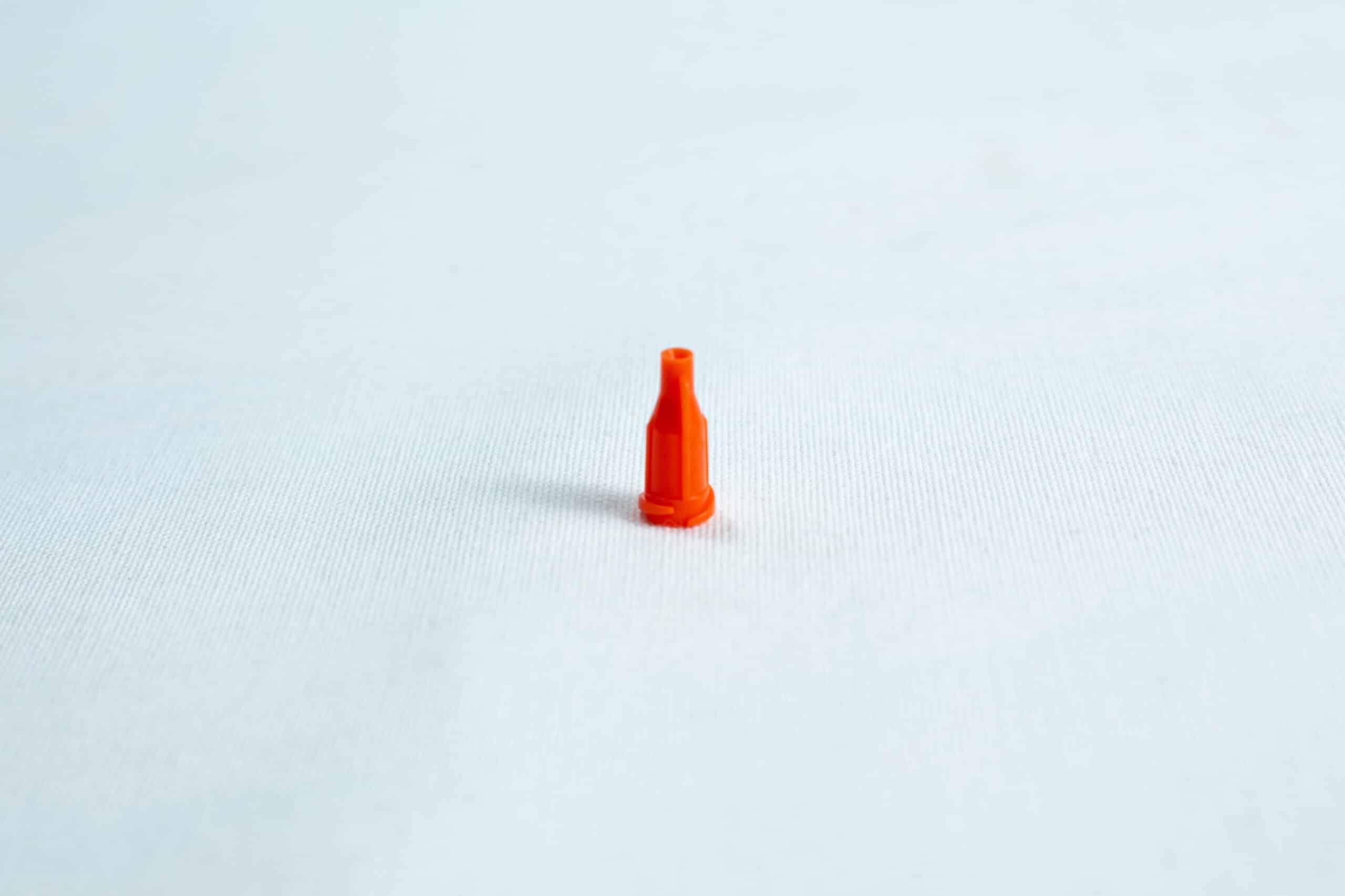 Syringe caps for Luer lock and slip tip 3 A small orange plastic nozzle stands upright on a plain white surface.