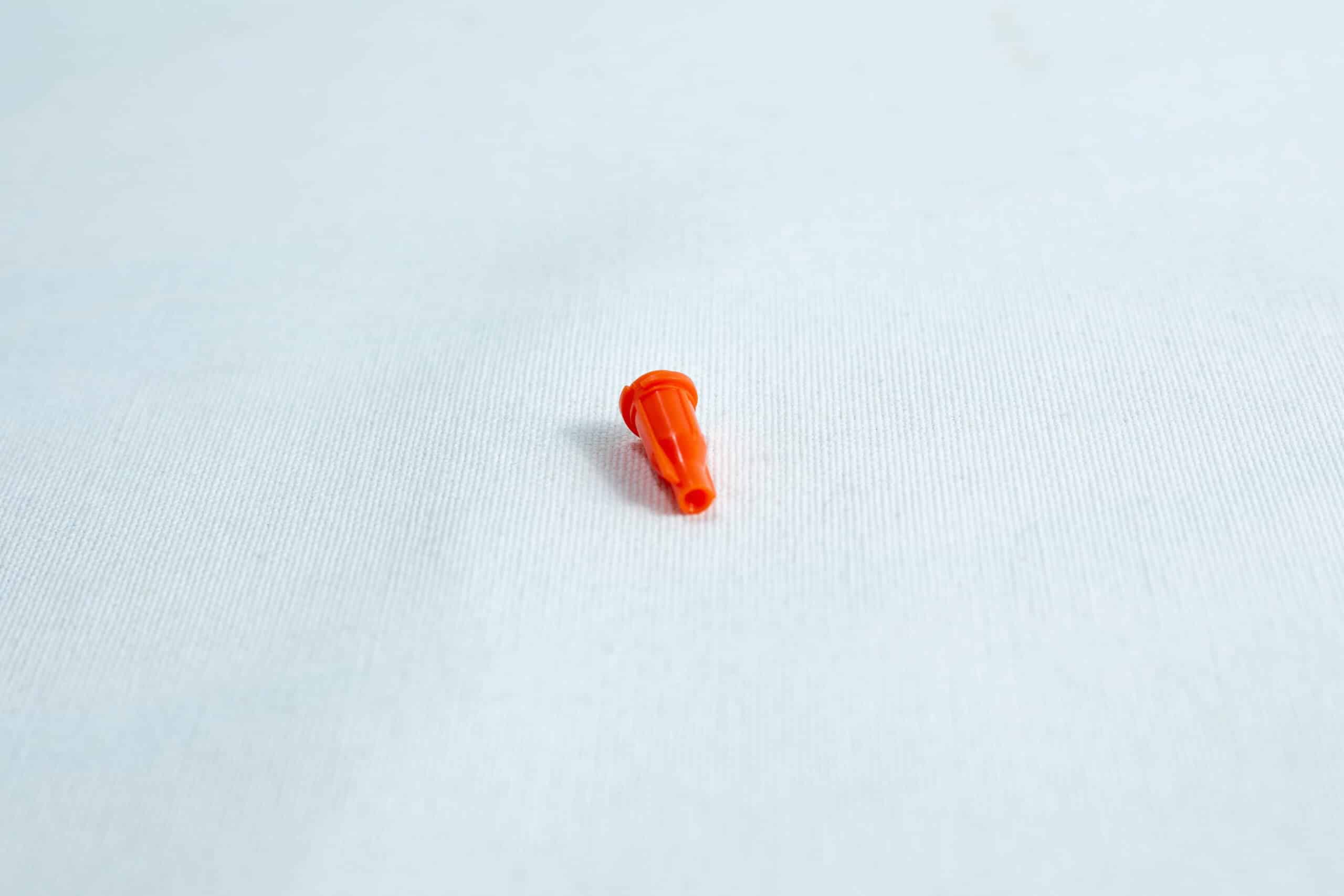 Syringe caps for Luer lock and slip tip 2 Small orange plastic object on a plain white surface.