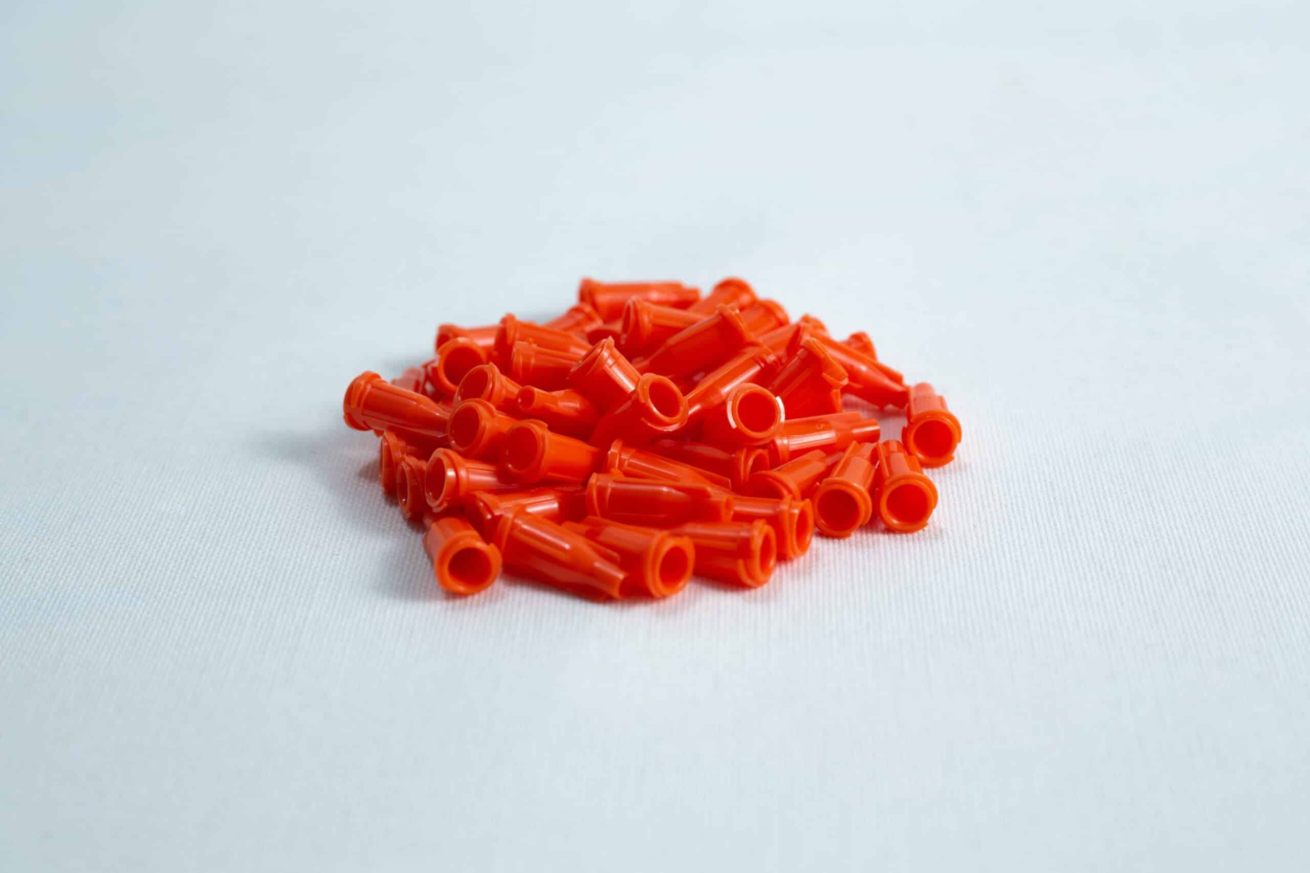 Syringe caps for Luer lock and slip tip 1 A pile of small, orange plastic caps on a white surface.