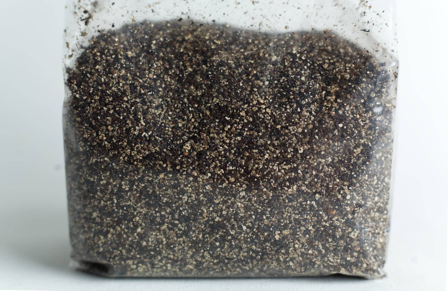 Mushroom Casing layer - Pasteurized or sterilized 1Kg 2 A clear plastic bag filled with coarse, dark soil or sand on a white surface.