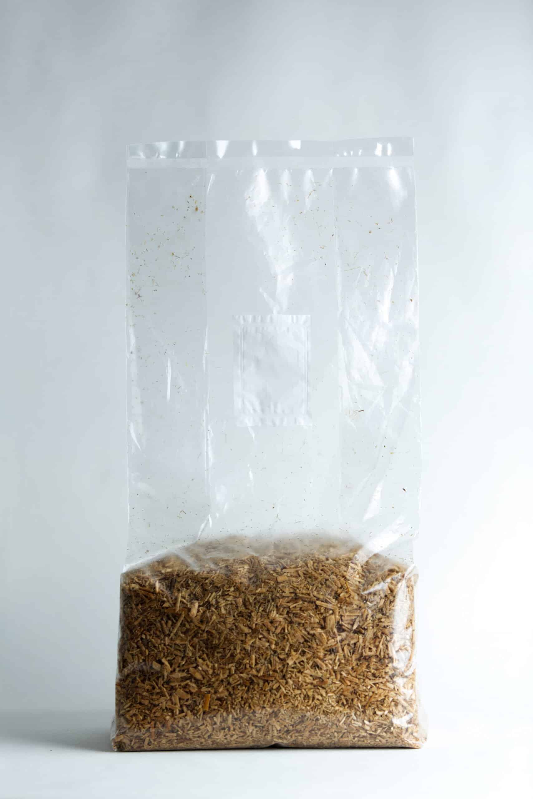 Hemp Substrate or Sawdust Substrate | Mycelium Growth Medium 4 A clear plastic bag filled with brown woodchips against a plain white background.