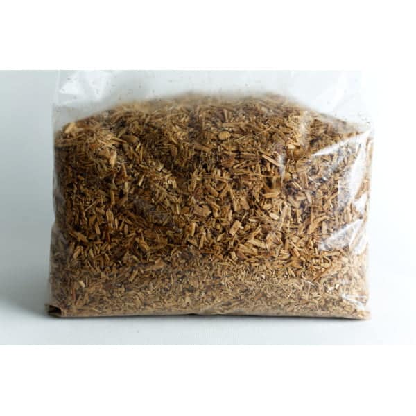 A clear plastic bag filled with chopped wood chips or shavings against a white background.