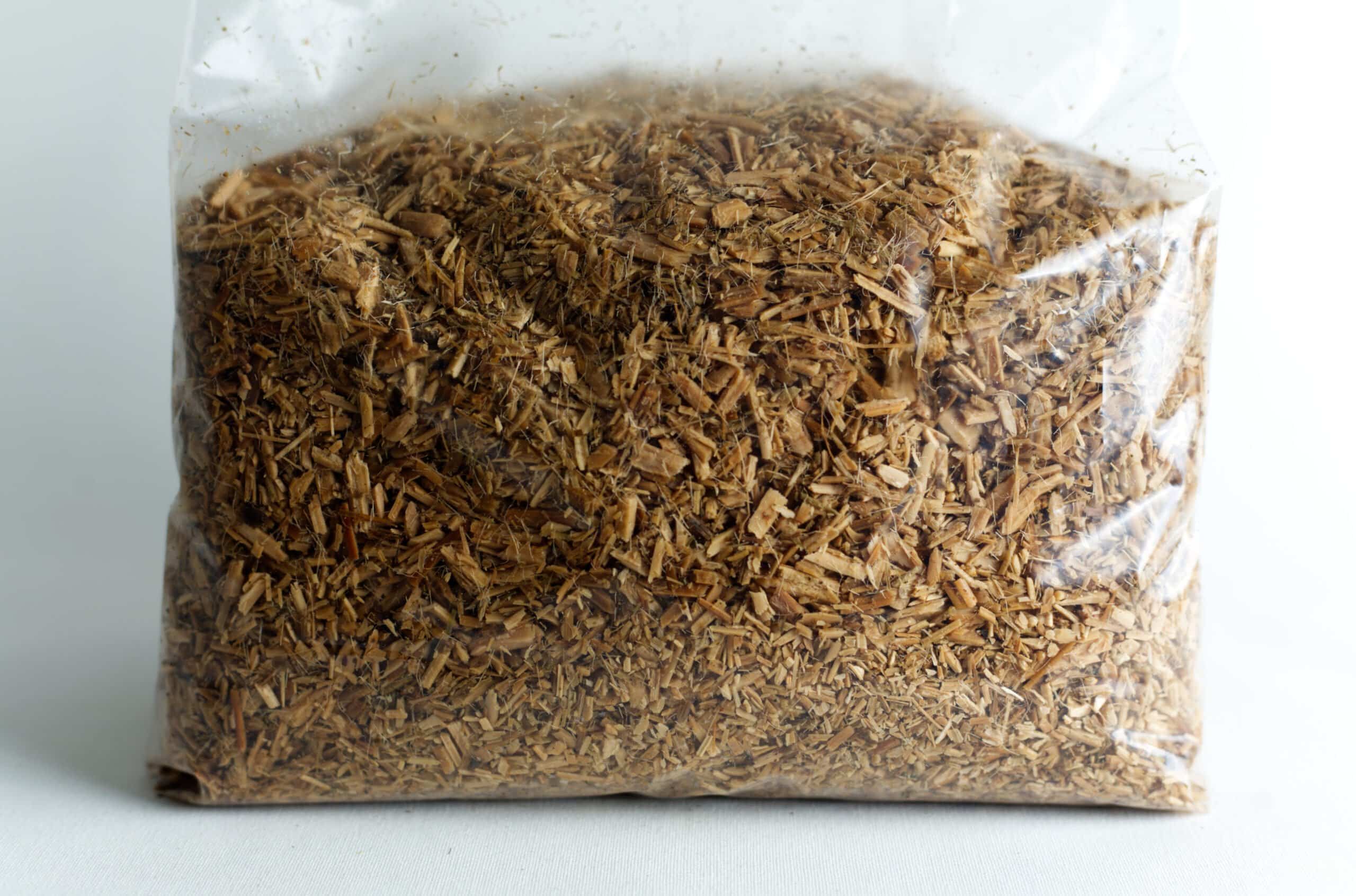 Hemp Substrate or Sawdust Substrate | Mycelium Growth Medium 2 A clear plastic bag filled with chopped wood chips or shavings against a white background.
