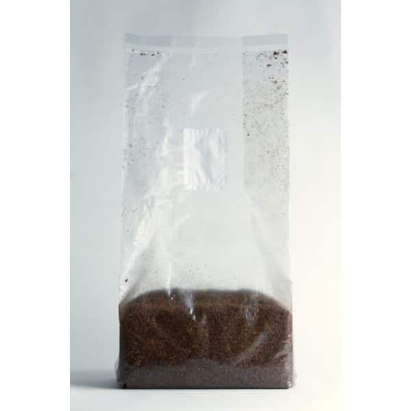 Clear plastic bag filled with brown coffee grounds against a plain background.