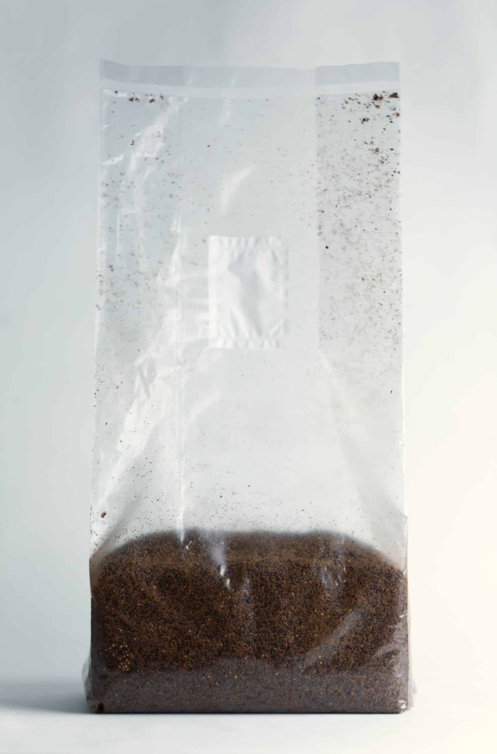 Hemp Substrate or Sawdust Substrate | Mycelium Growth Medium 3 Clear plastic bag filled with brown coffee grounds against a plain background.