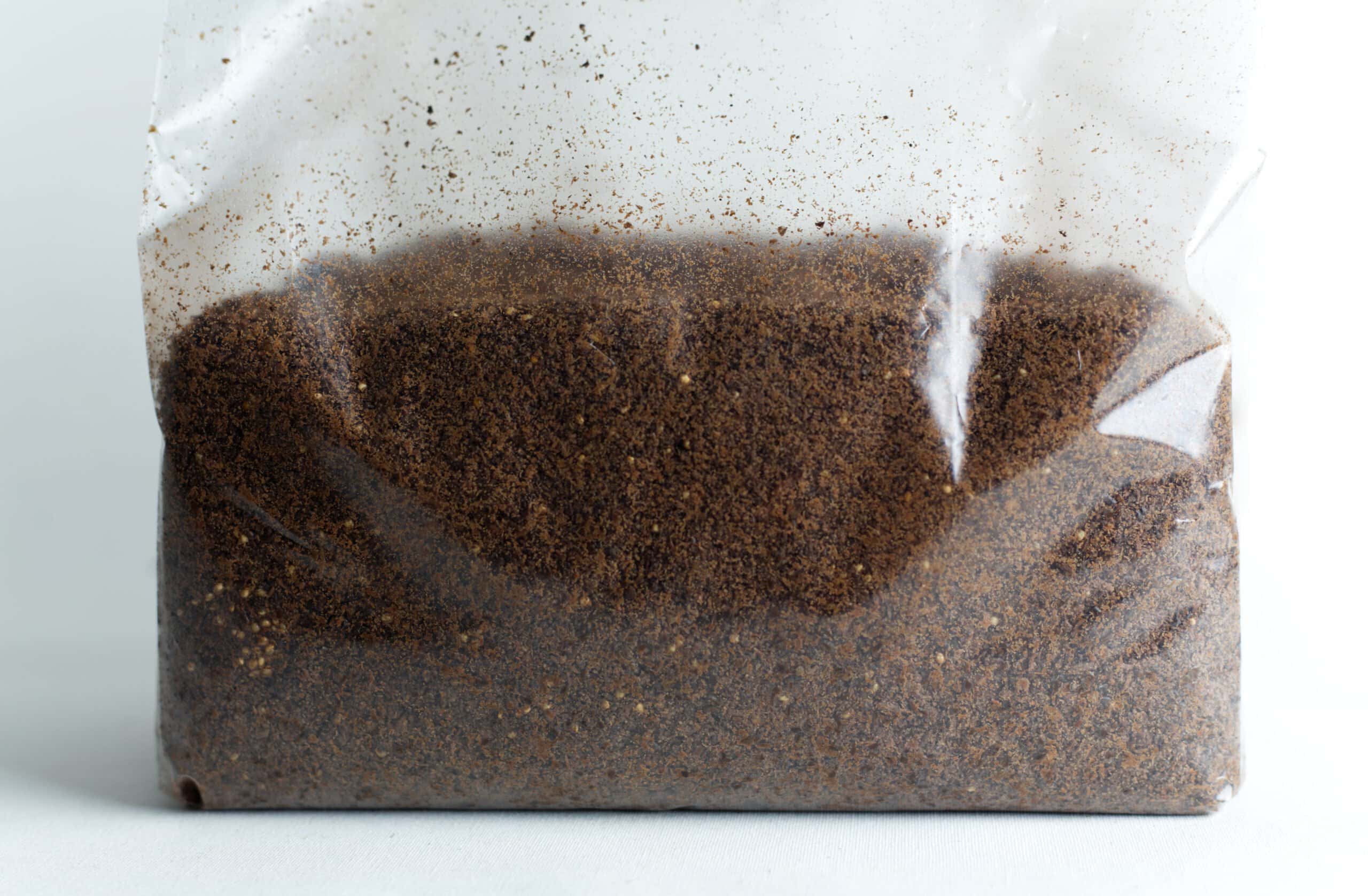 Hemp Substrate or Sawdust Substrate | Mycelium Growth Medium 1 Clear plastic bag filled with brown ground coffee against a white background.