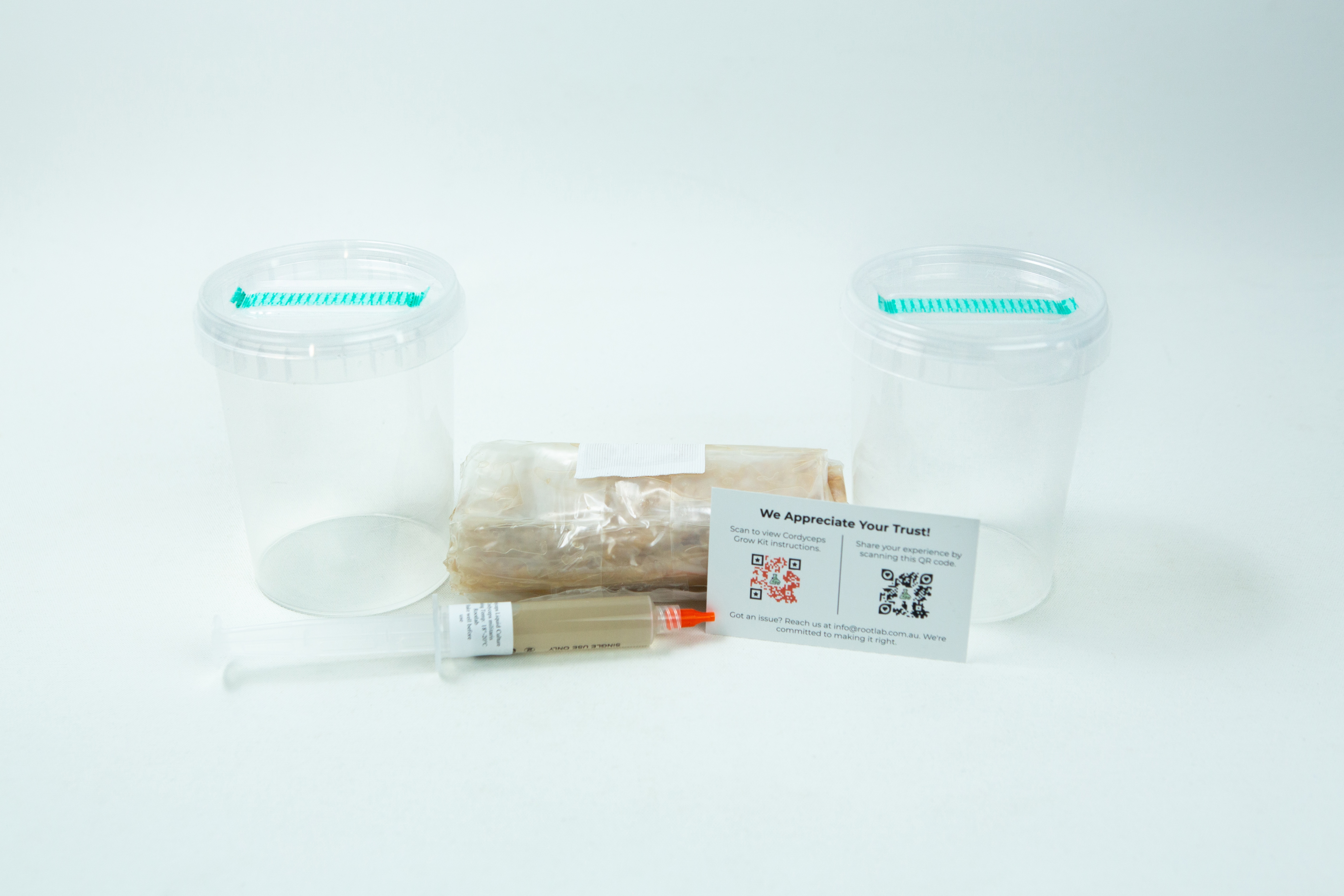 Cordyceps militaris Mushroom Grow Kit 1 Two empty plastic containers, a wrapped item, syringe, and info card from the Cordyceps militaris Mushroom Grow Kit are arranged on a white background.