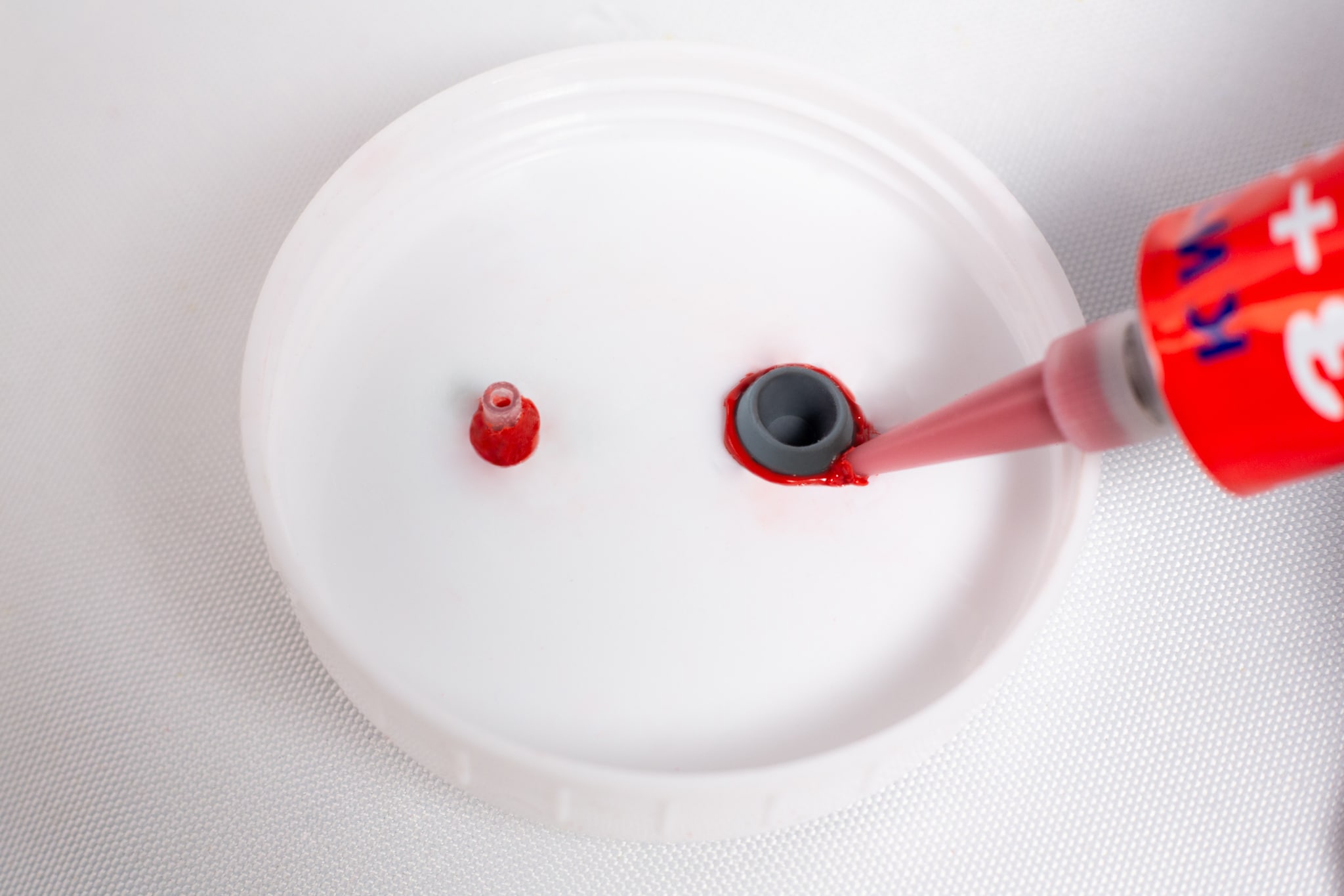 High Temperature RTV Silicon-Red 5 High Temperature RTV Silicone-Red is being applied around a grey nozzle on a white plastic surface.