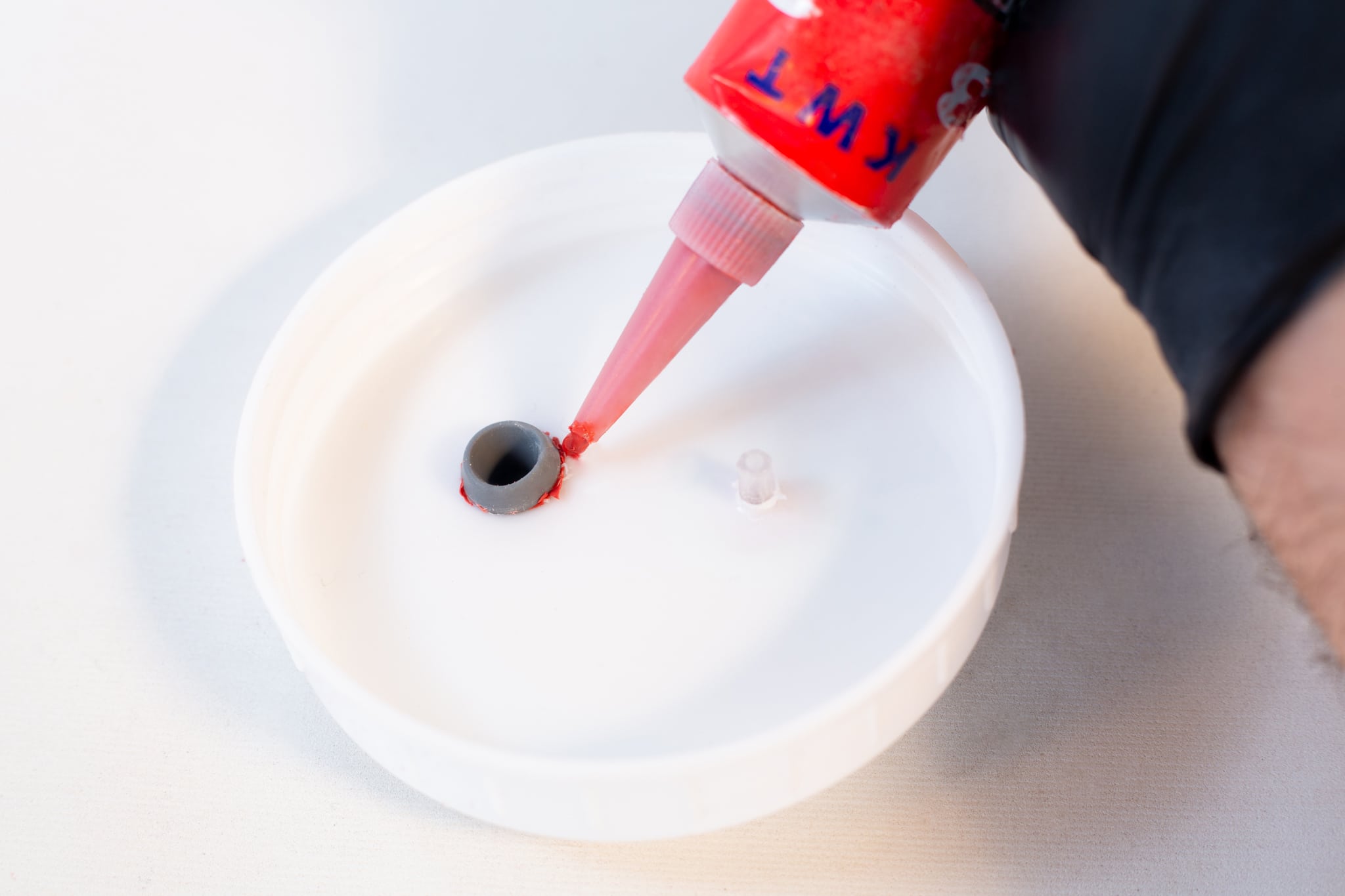 High Temperature RTV Silicon-Red 4 A person dispenses High Temperature RTV Silicone-Red through a nozzle into a small hole of a white circular container, preparing it for sealing.
