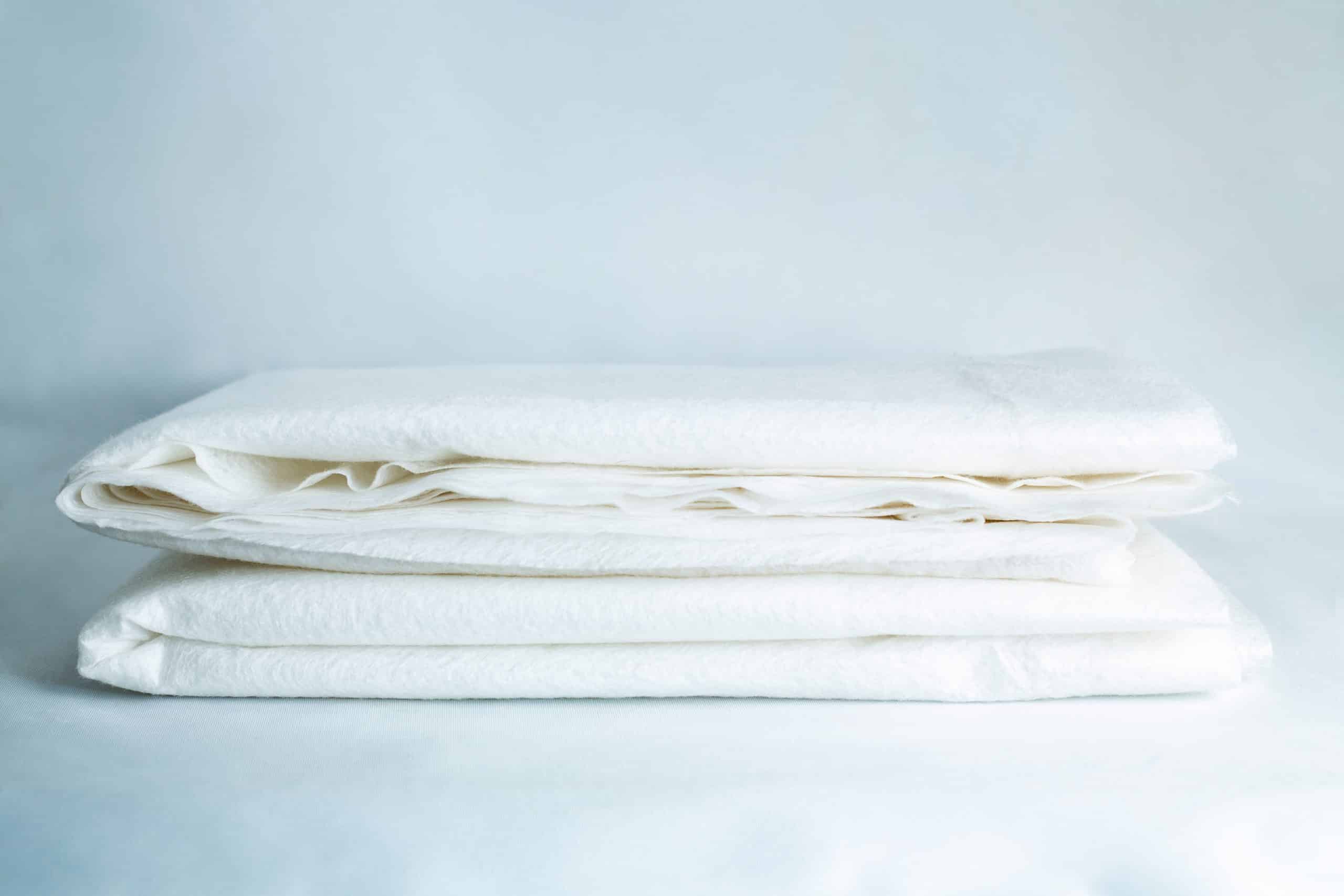 Light Log Blanket 1 Two neatly folded white bed sheets rest on a light surface with a soft blue backdrop, making them an ideal match for the Light Log Blanket.