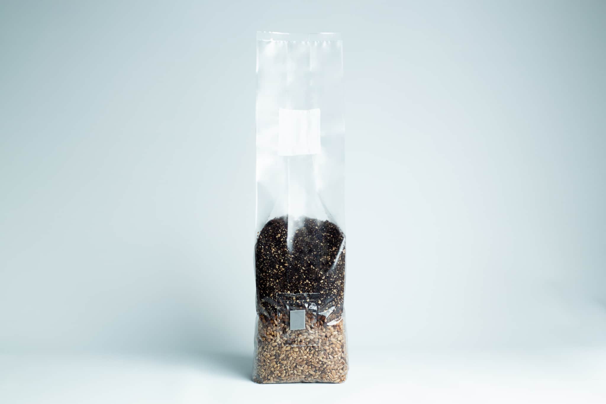 All in one Coco Coir+Vermiculite | organic rye | Millet | 1kg | 2kg Mushroom bag | Instruction 6 A clear plastic bag filled with brown and black seeds, standing upright on a light surface.