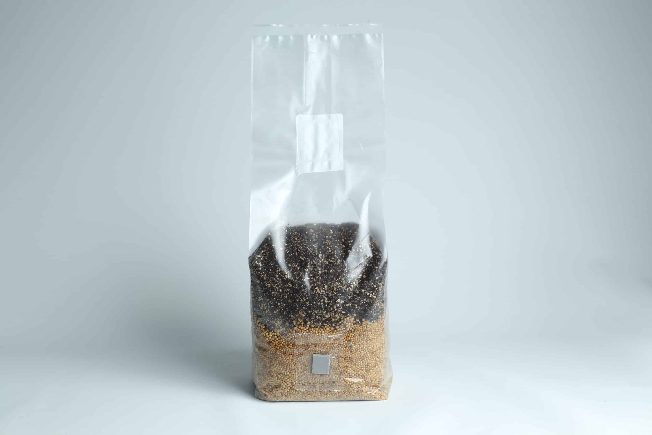 All in one Coco Coir+Vermiculite | organic rye | Millet | 1kg | 2kg Mushroom bag | Instruction 8 A clear plastic bag filled with black and brown grains on a plain white background.