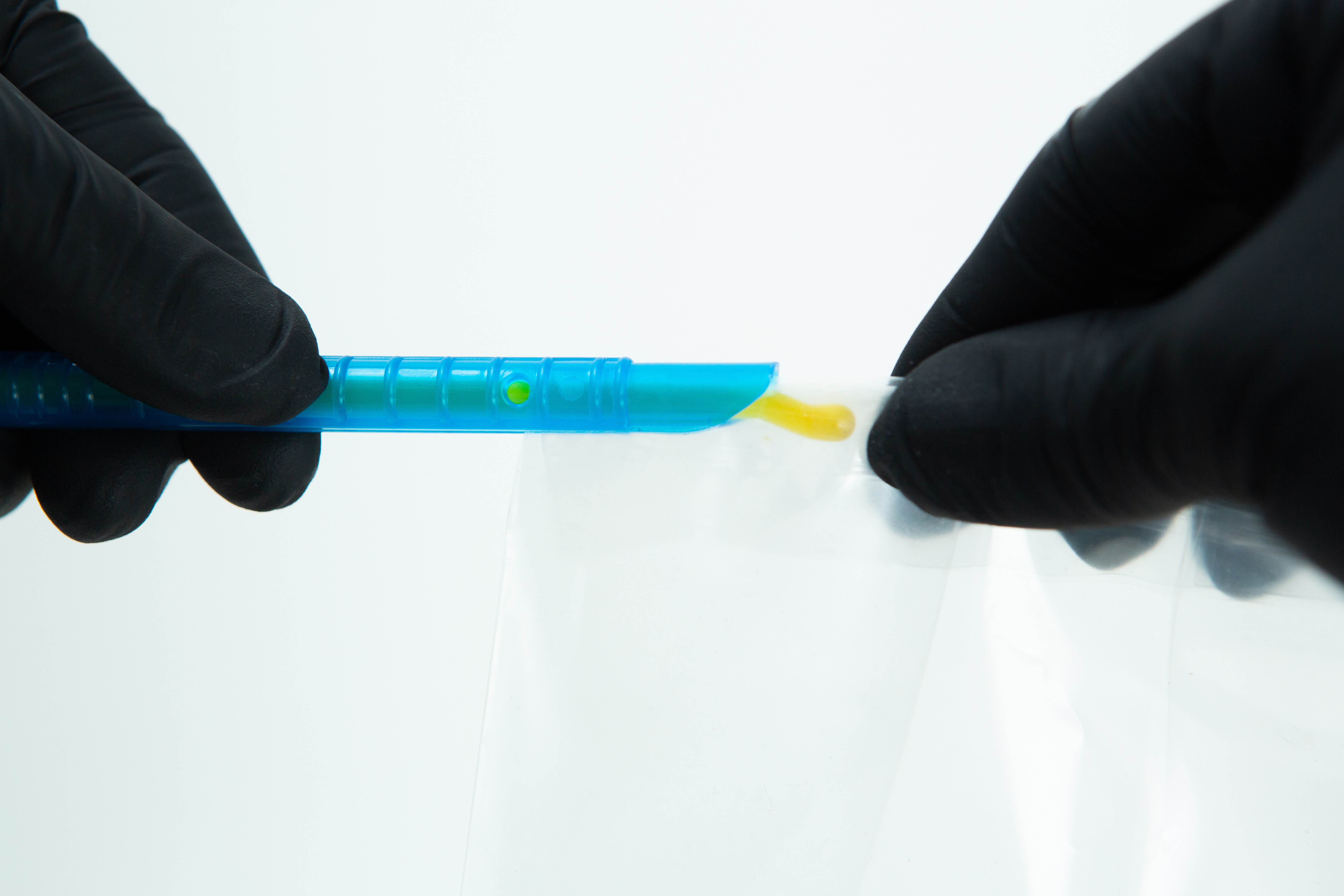 Mushroom bag sealing clip | Reusable 2 Gloved hands handling a blue plastic tool with yellow substance over a clear plastic bag.