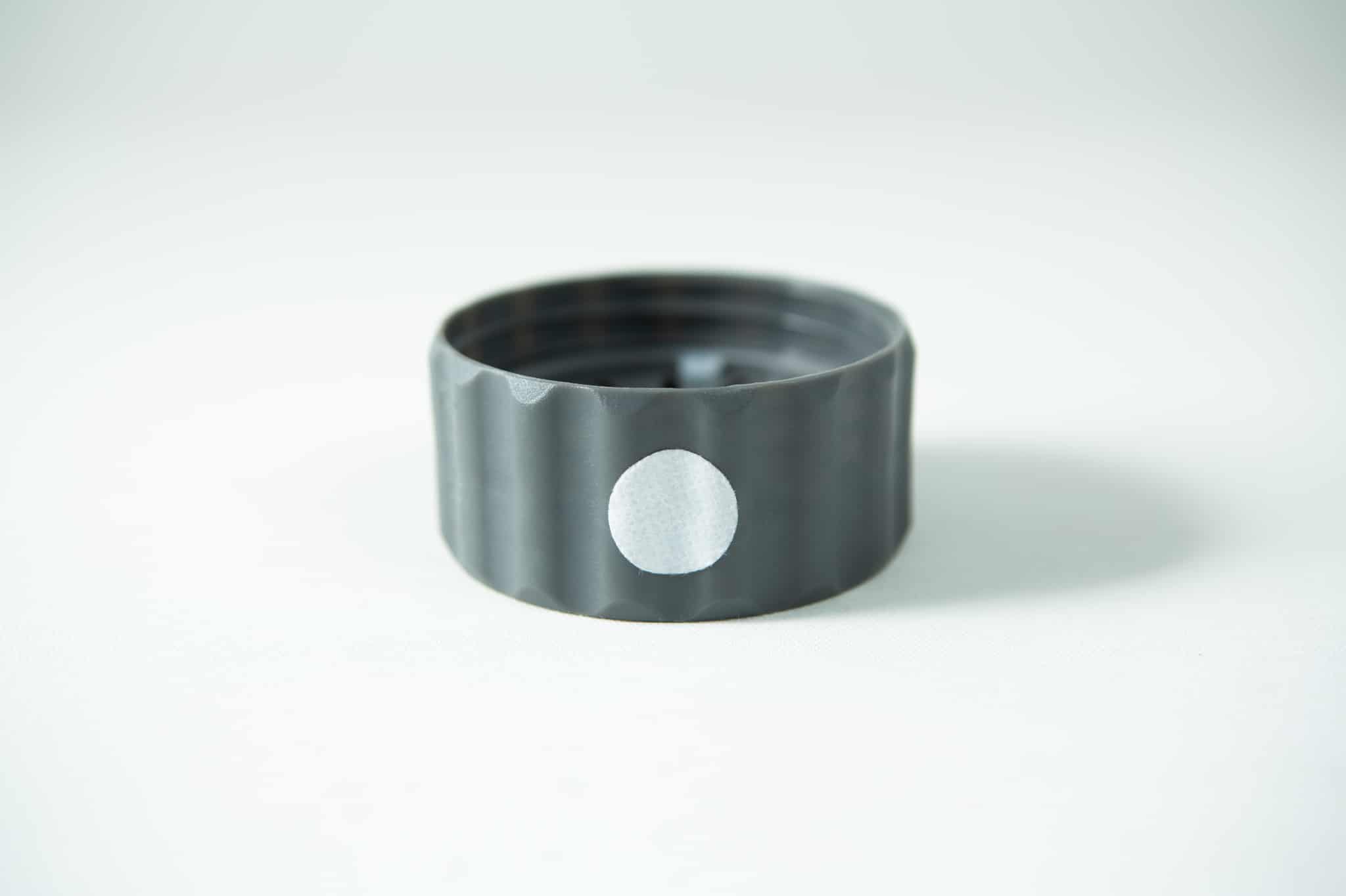 Plant Cell Biocoupler™ collar only (regular mouth) 1 A Plant Cell Biocoupler™ Glass Set bottle cap—grey plastic with a white circular sticker on its side—rests on a white surface.