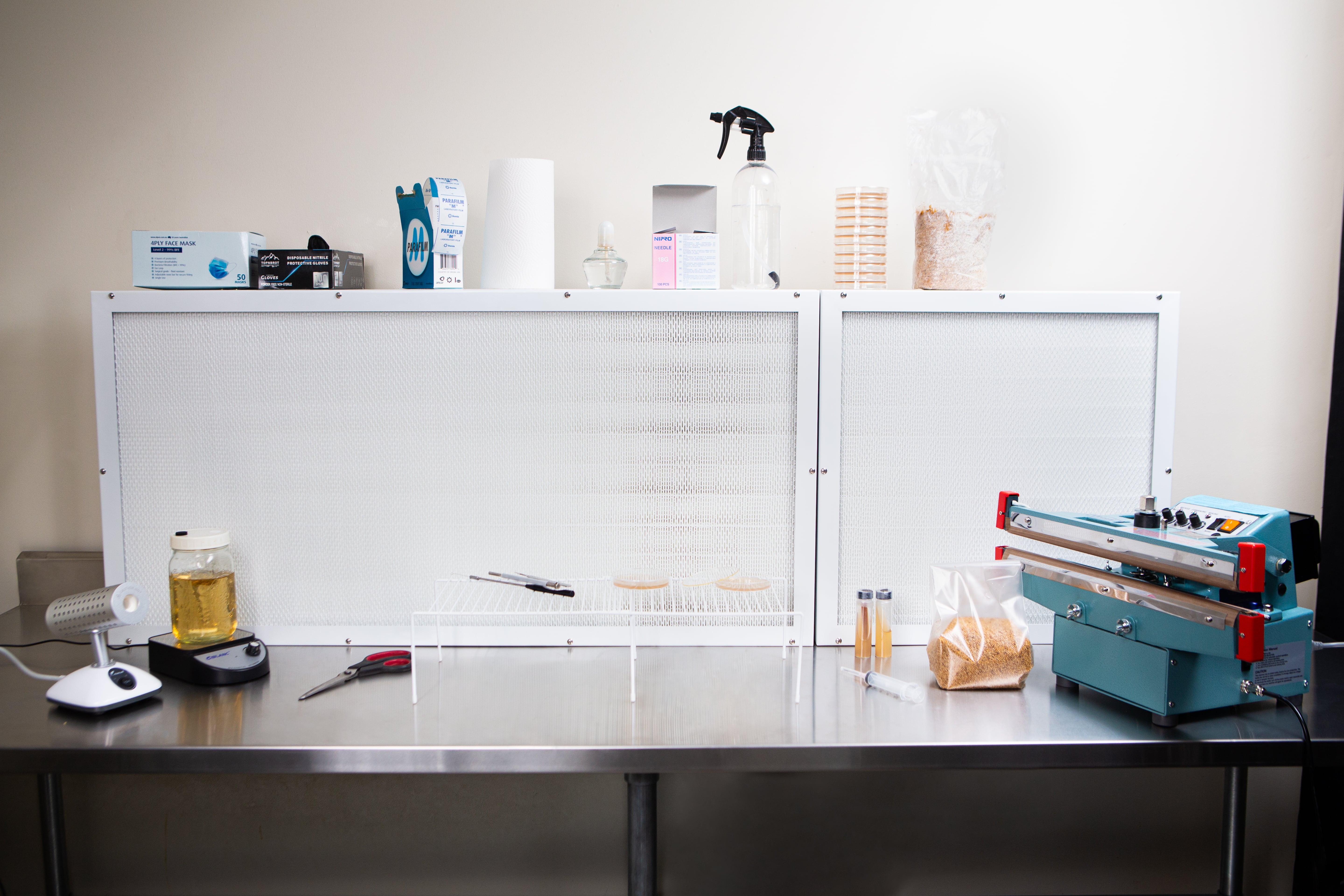 Laminar Flow Hood HEPA Airfilter H14 w/prefilter 60x60x35cm 5 A clean lab workspace features a Laminar Flow Hood HEPA Airfilter H14 with pre-filter 60x60x35cm, equipment, petri dishes, jars, and a vacuum sealer on a stainless steel table.